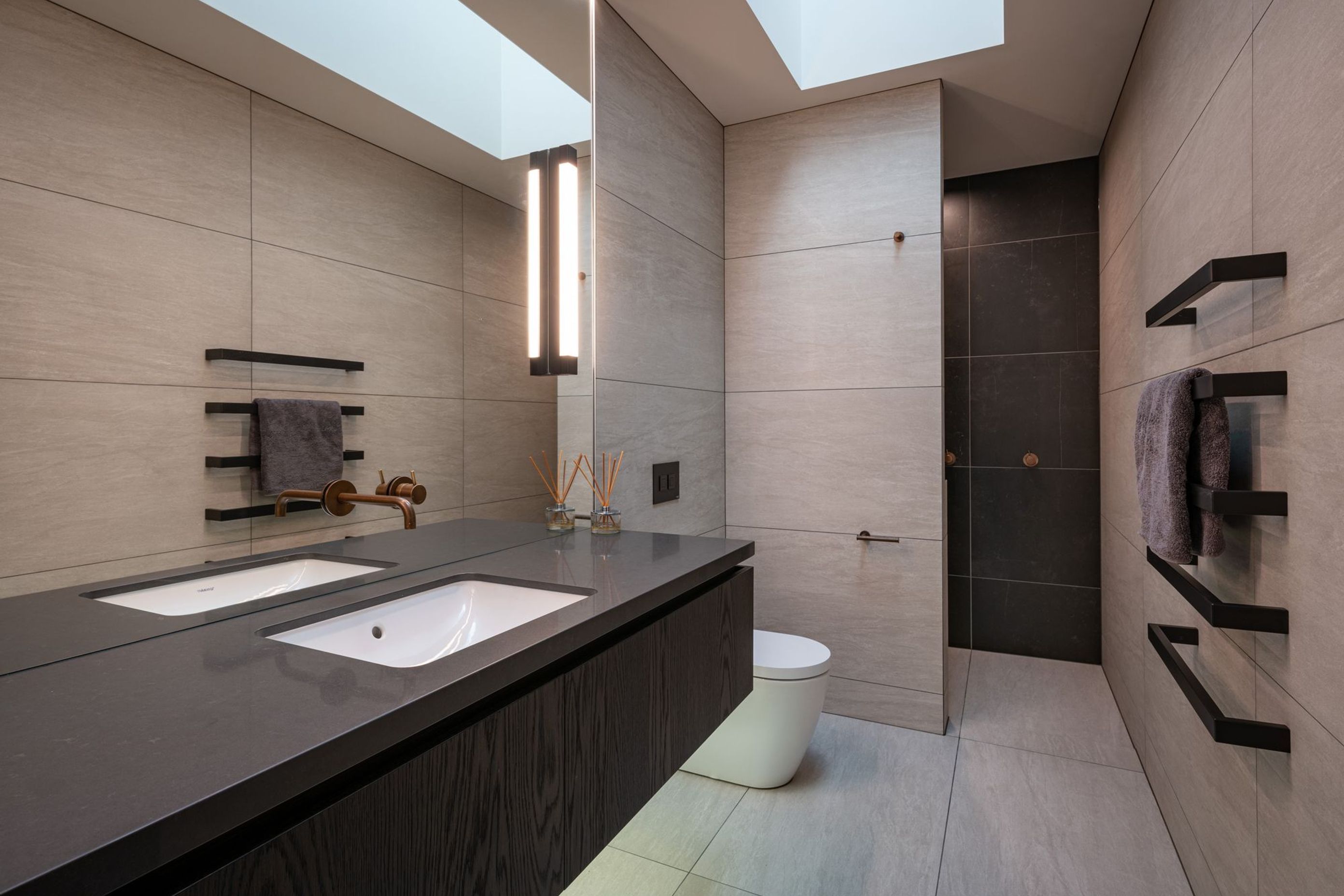 The family bathroom takes light in through a skylight and features dramatic monochromatic floor-to-ceiling tiles.