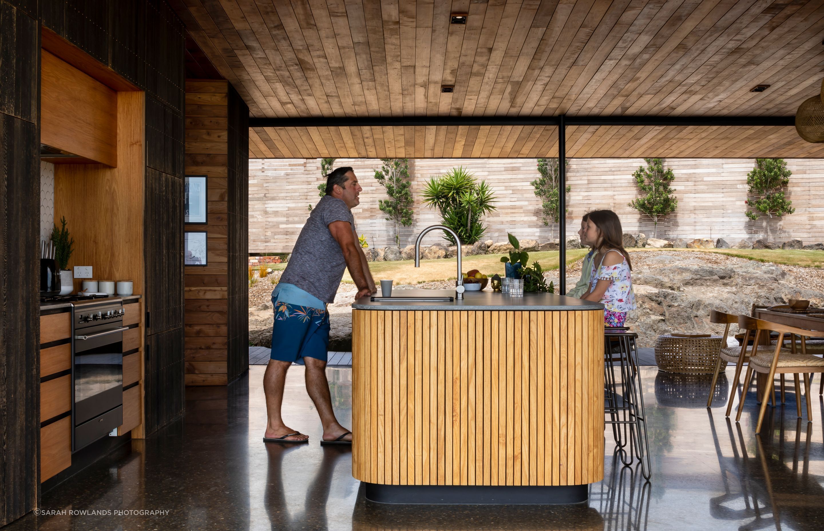 Ken serves his daughters at the kitchen island; the family home has spectacular indoor-outdoor flow for ease of family life.