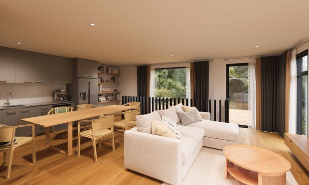 Open-plan contemporary living, dining and kitchen area with warm timber flooring and furniture, a neutral upholstered sectional sofa, built-in grey cabinetry, timber dining table and chairs, and large glazed openings with dark curtains and black vertical balustrade elements. The space is softly lit and connected to an outdoor balcony or terrace.