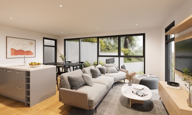 Contemporary open-plan living area combining a compact kitchen, dining zone and lounge. The room features warm timber flooring, light neutral walls, dark-framed glazing, a pale stone kitchen island, built-in timber media cabinetry, a large neutral sectional sofa and a round coffee table. Abundant windows provide a bright connection to an enclosed garden or courtyard.