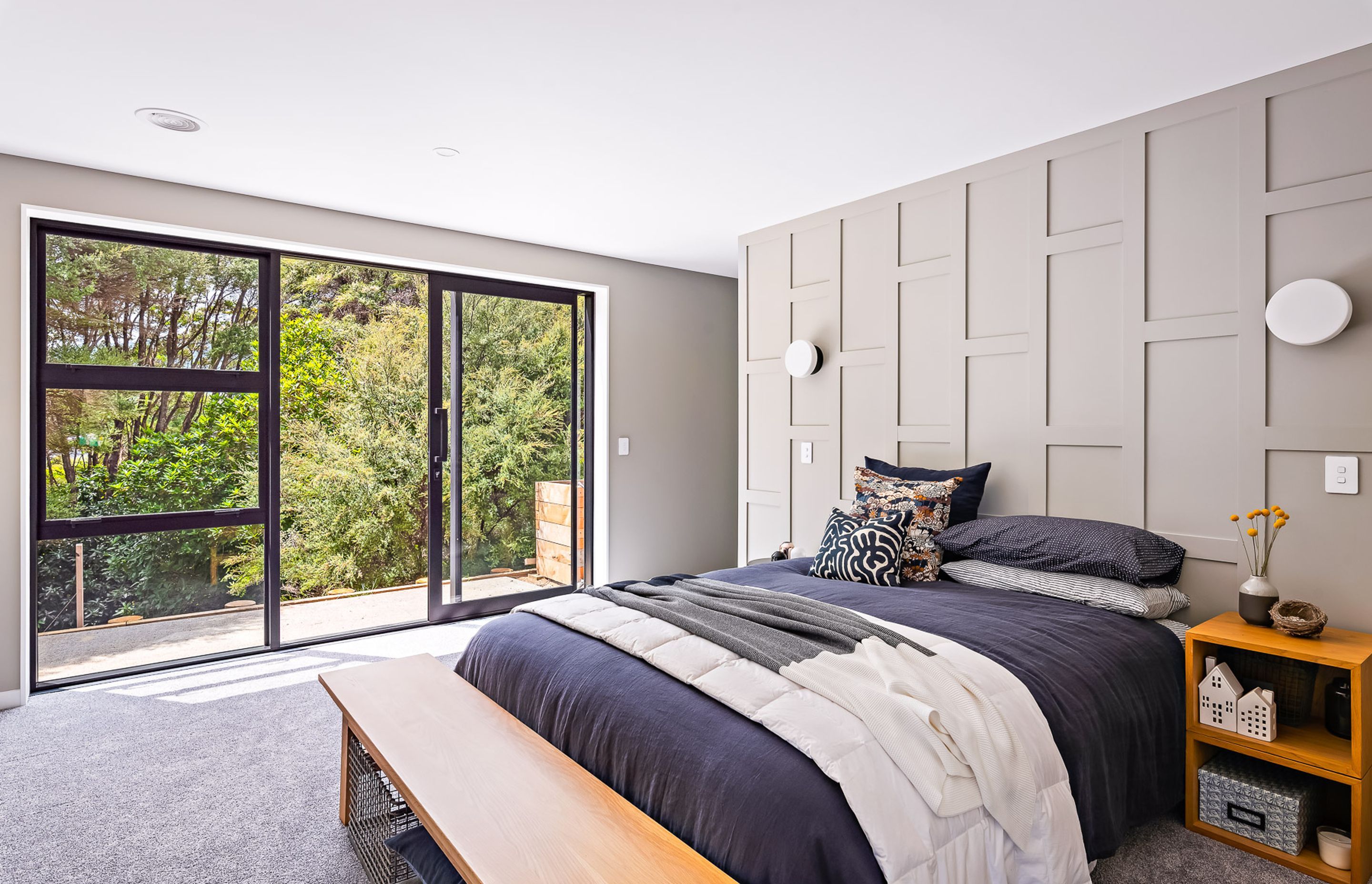 The main bedroom enjoys a backdrop of native kānuka and opens out onto a private courtyard space for morning sun.