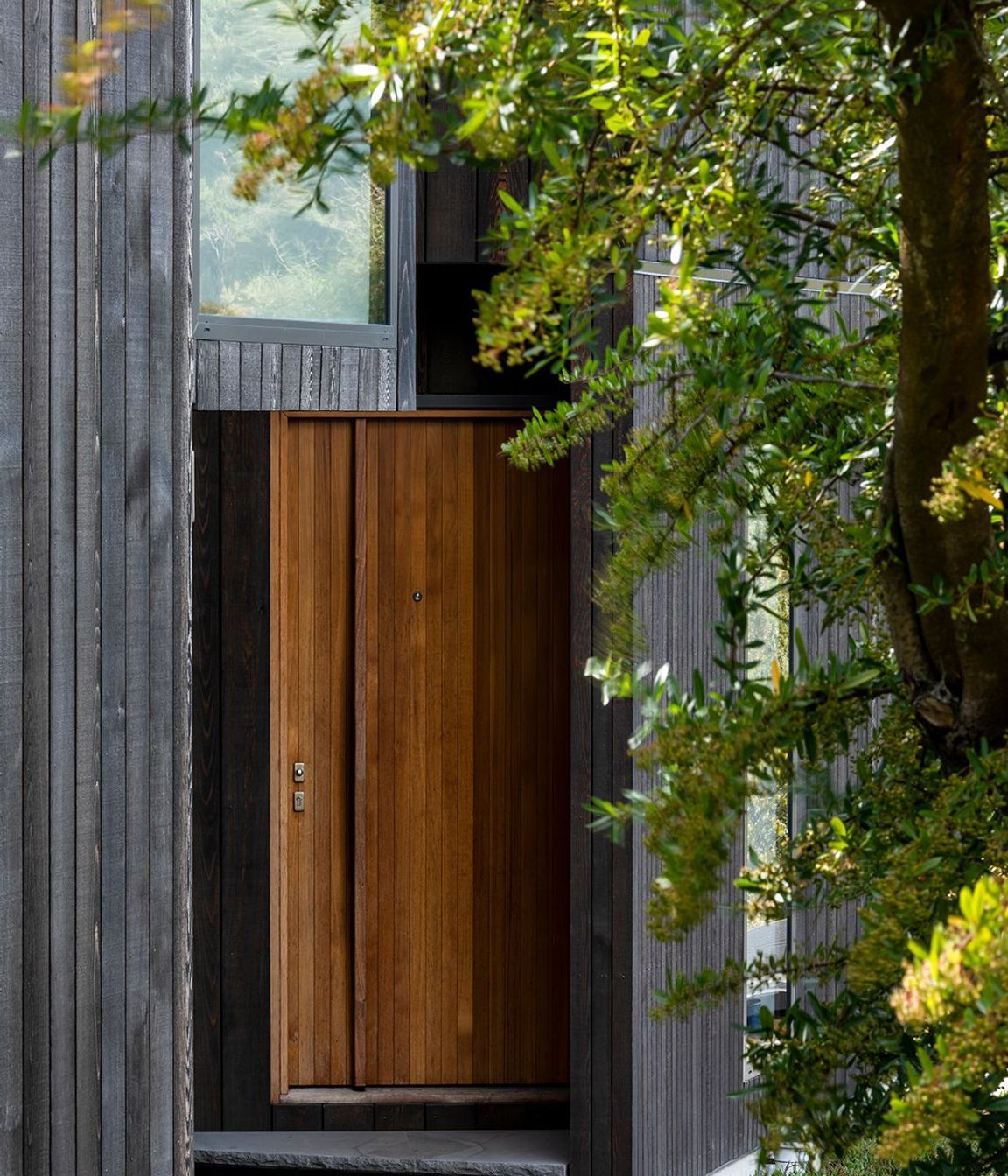 The discreet entryway is folded into the house, with a contrasting stain front door to mark the entrance.