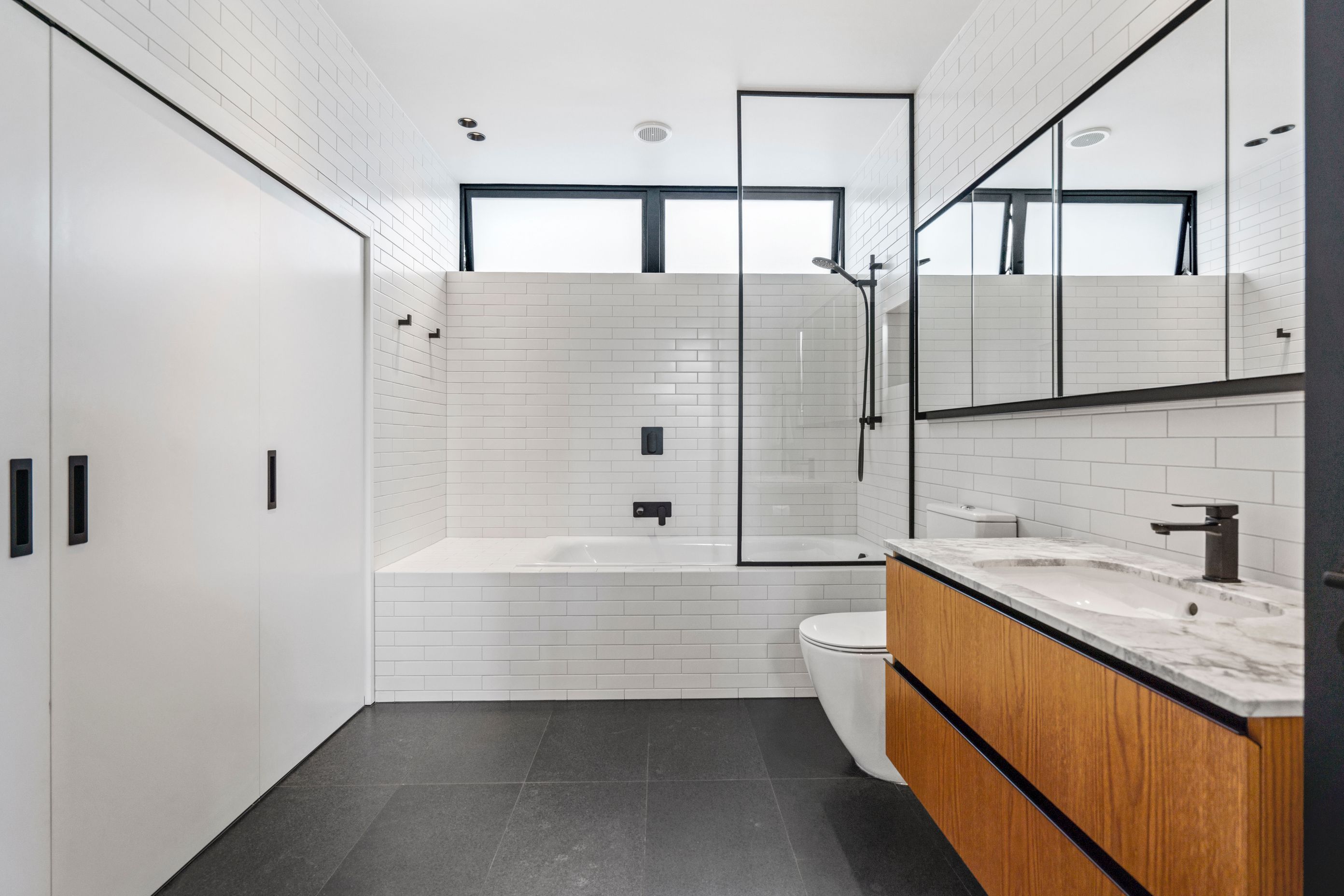 The bathroom has a modern-classic feel with on-trend subway tiling from floor to ceiling, coupled with black tapware and wooden cabinets.