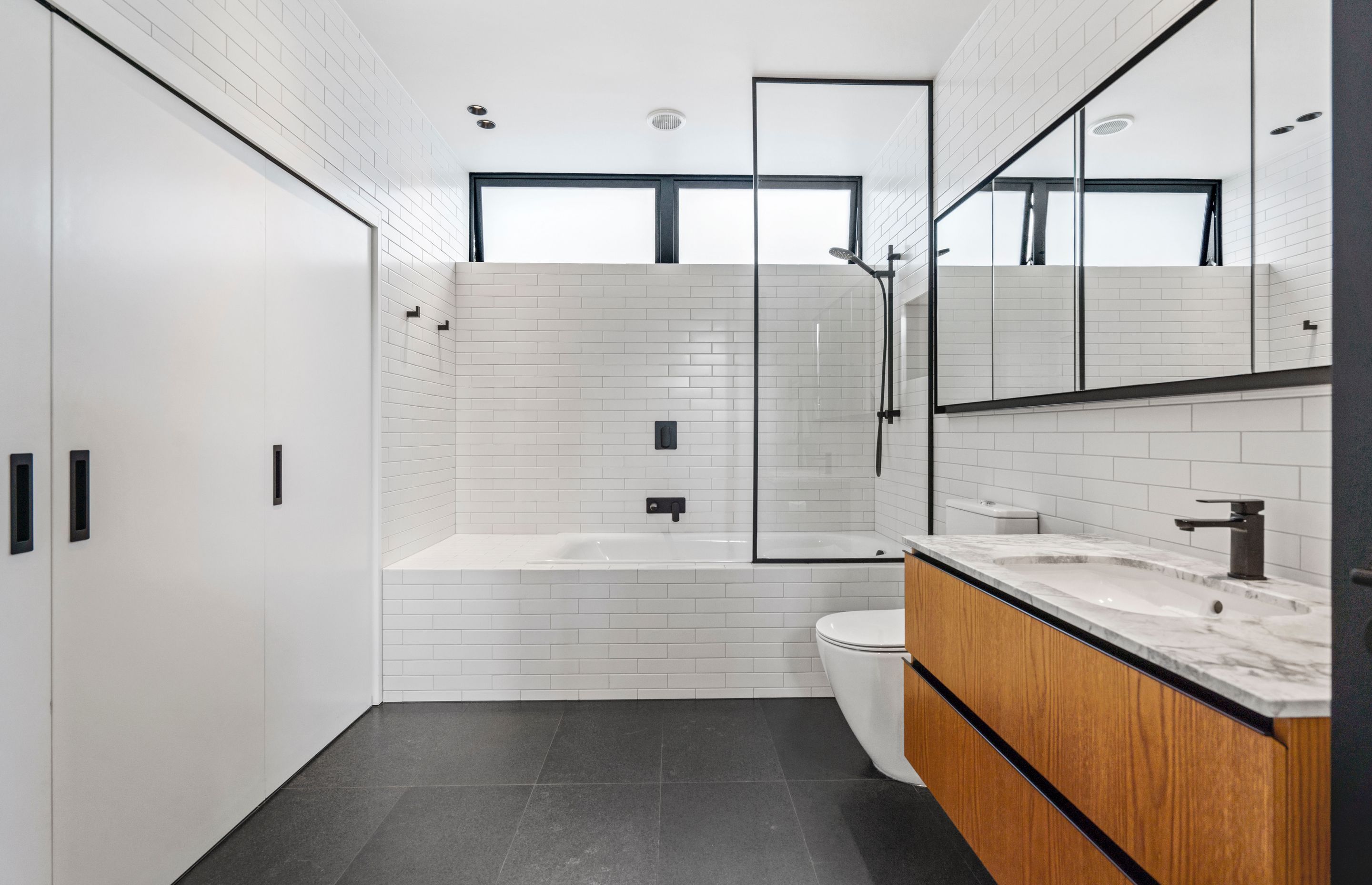 The bathroom has a modern-classic feel with on-trend subway tiling from floor to ceiling, coupled with black tapware and wooden cabinets.