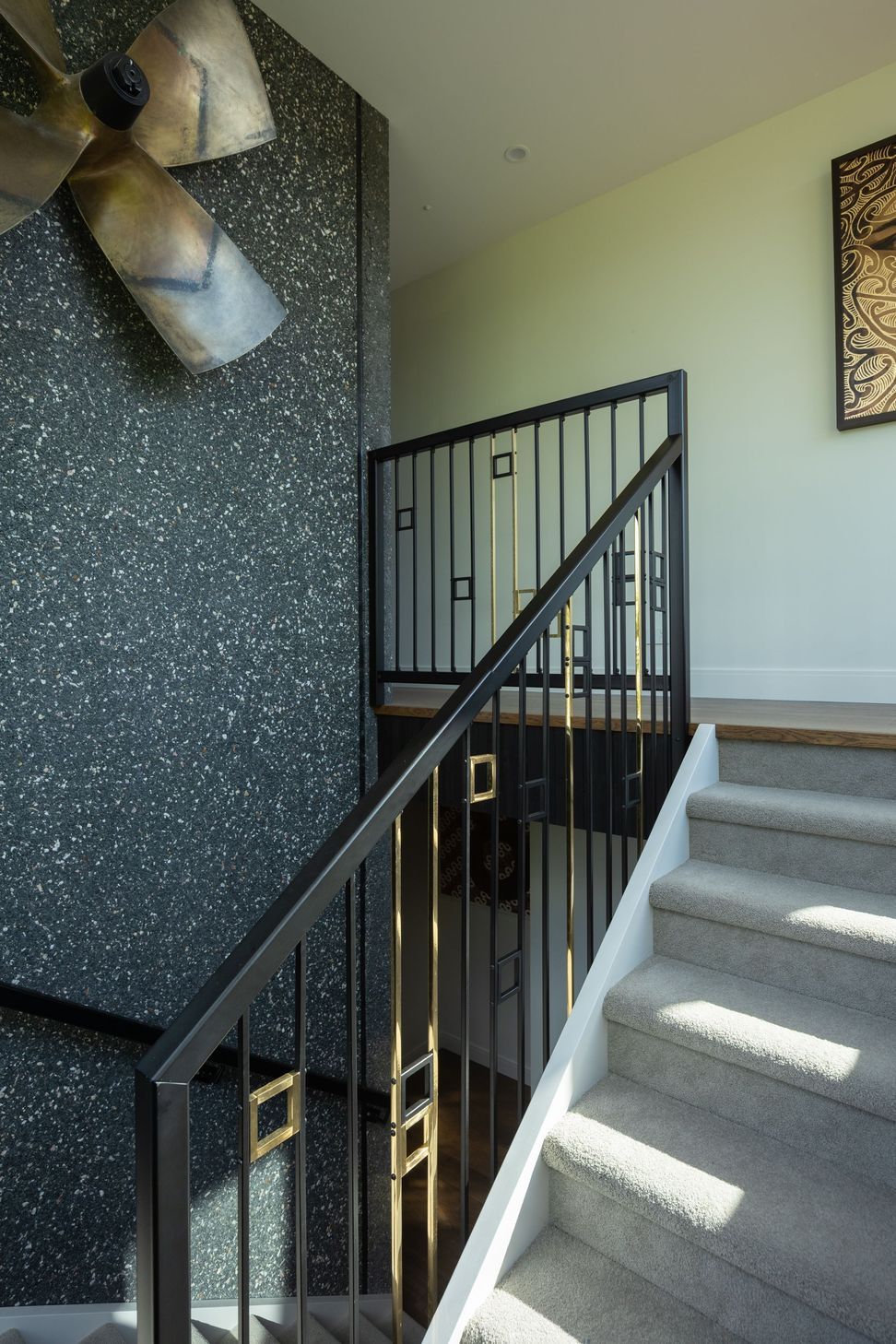 The internal staircase celebrates the beauty of honest materials, pairing exposed tilt slab concrete with visible aggregate against crisp black steel balustrades. The sculptural stair becomes a defining architectural feature within the home.