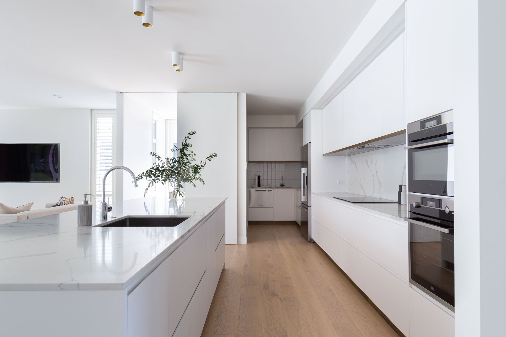 The kitchen's streamlined, white and marble materiality enhances the elegance and minimalism of the space.
