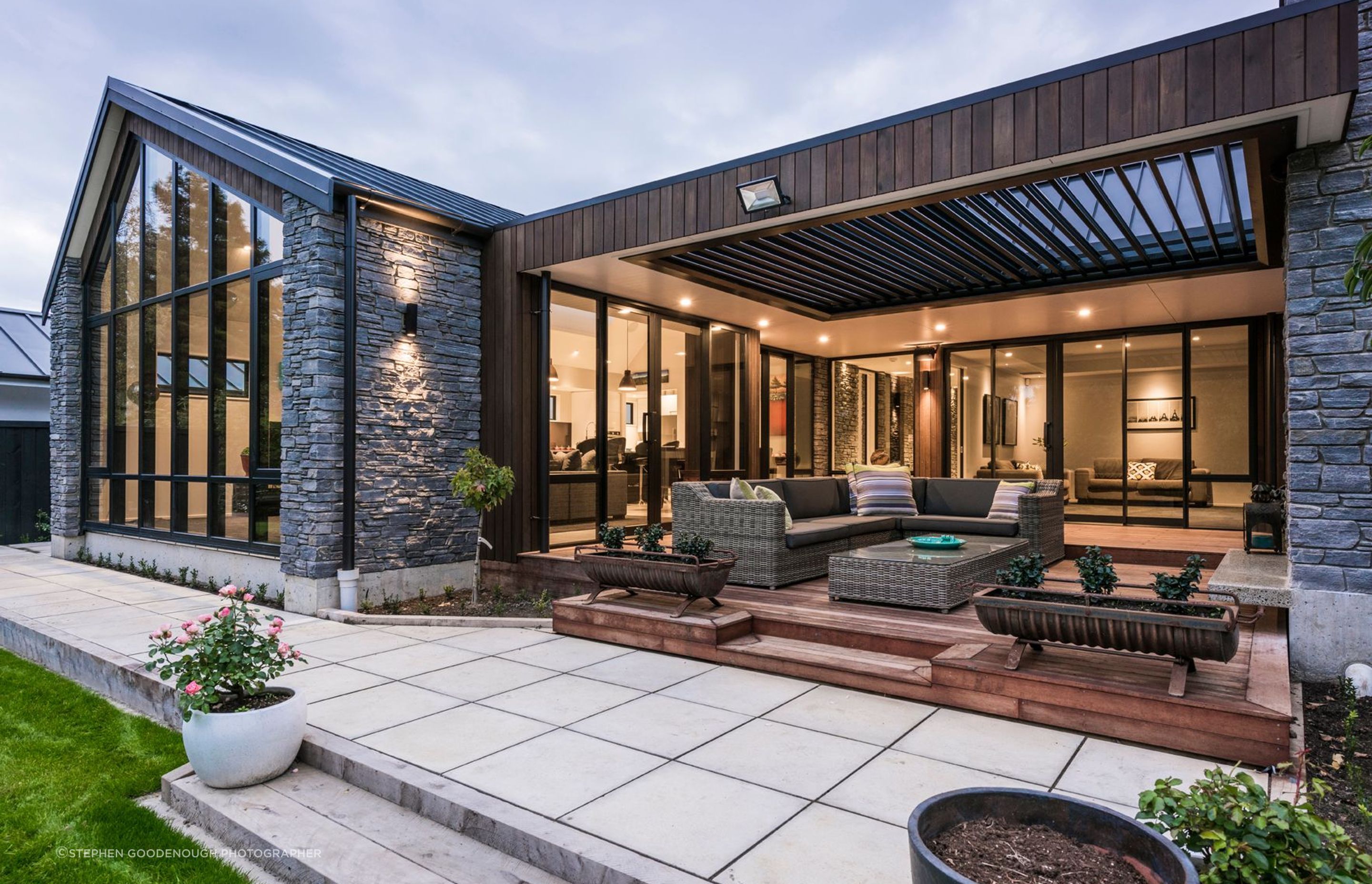 The electric louvred outdoor living area features  a stone fireplace and directly enjoys the view of the stream.