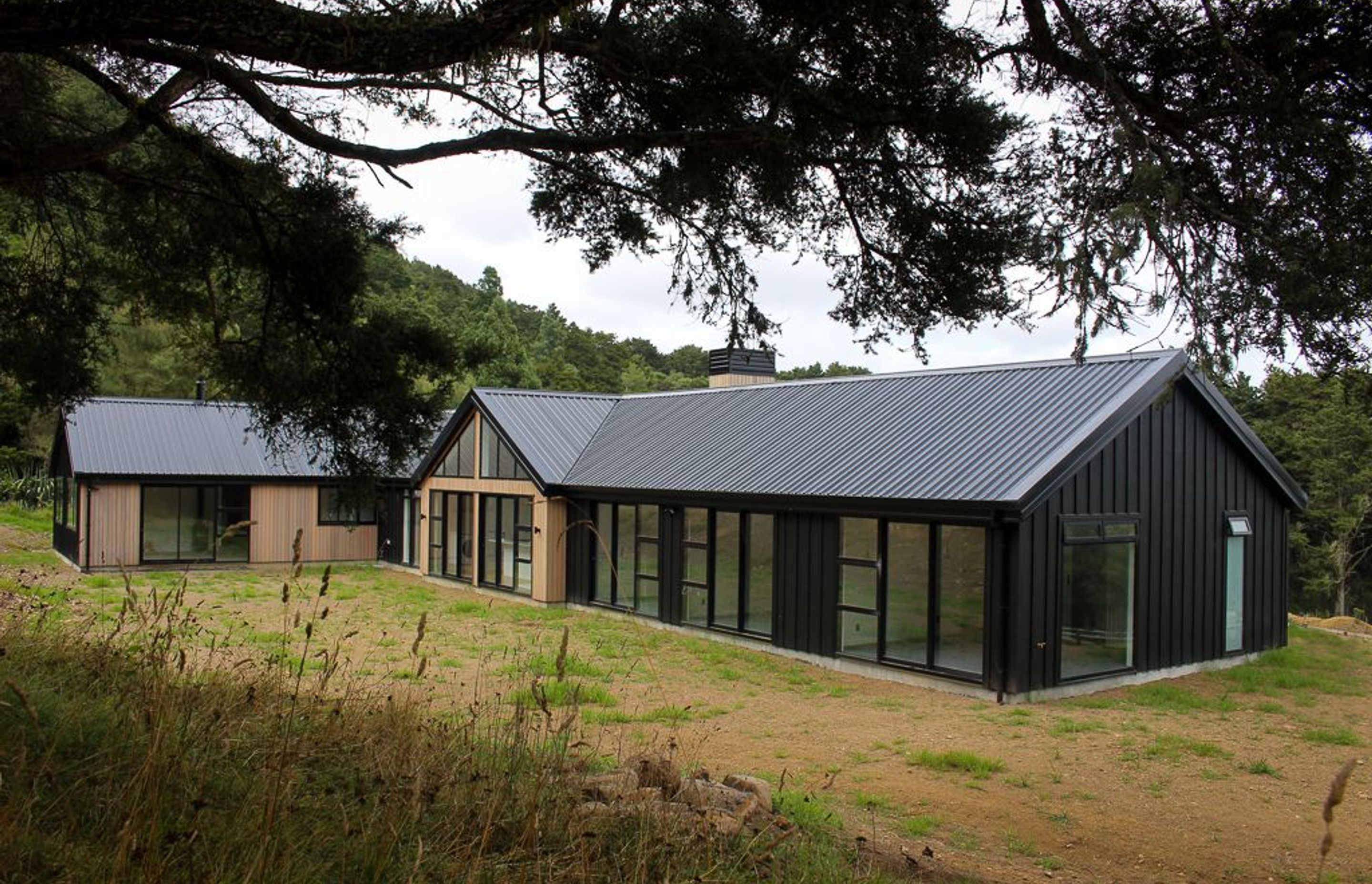 Clad in black Triclad board & Batten with Cedar gables & a custom built cedar clad chimney with powdercoated cowling. This family home sits proudly in its rural setting. Visible on the left is a fully self contained unit for extended family.