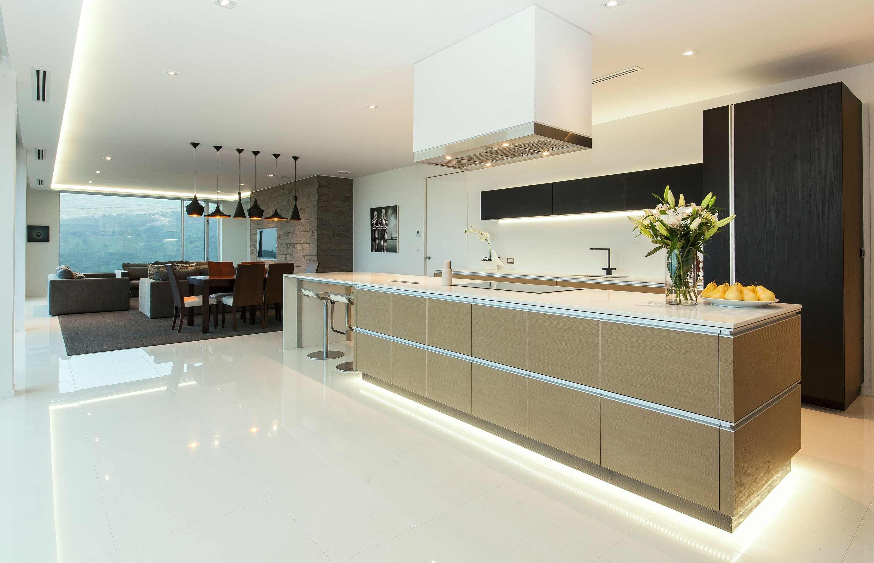 Recessed lighting around the ceiling and beneath the high-level cabinetry and island bench adds a subtle visual note, playing off the highly polished surface of the floor and more matte walls and ceiling planes.