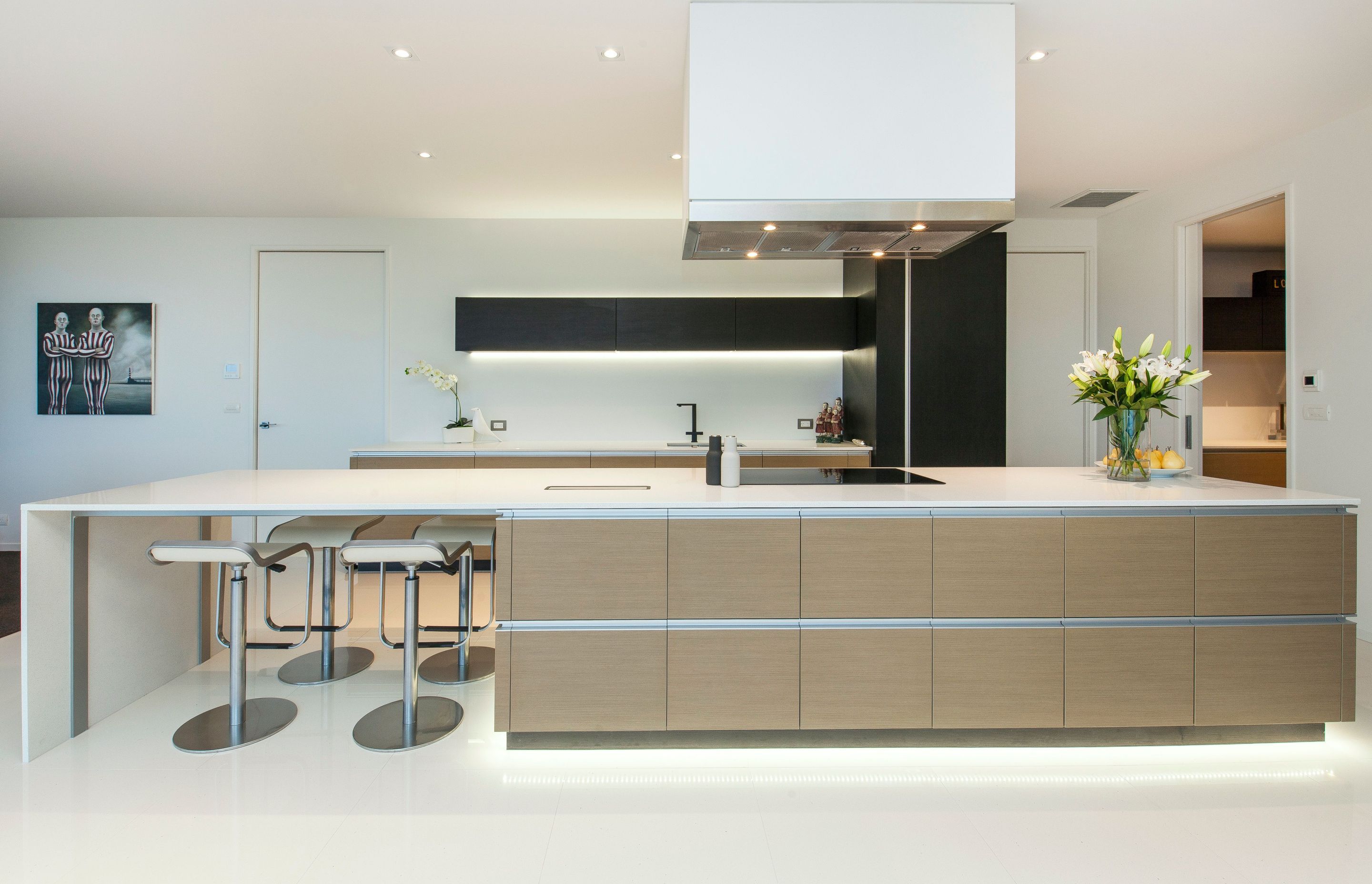 In keeping with the form of the house, the large island bench is low and wide with a mix of horizontal and vertical lines, which have been picked up in the wall cabinetry and also in the scullery.