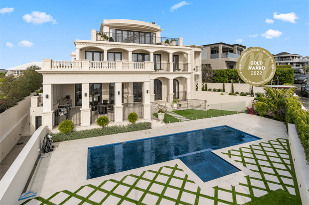 A grand multi-storey cream-coloured residence with classical detailing, arched openings, balustrades, columns and extensive balconies. The property is viewed from above across a landscaped courtyard with a large geometric swimming pool, pale paving, clipped planting and lawn lattice patterns. A rooftop terrace and neighbouring apartment buildings are visible in the background, along with an award badge overlay.