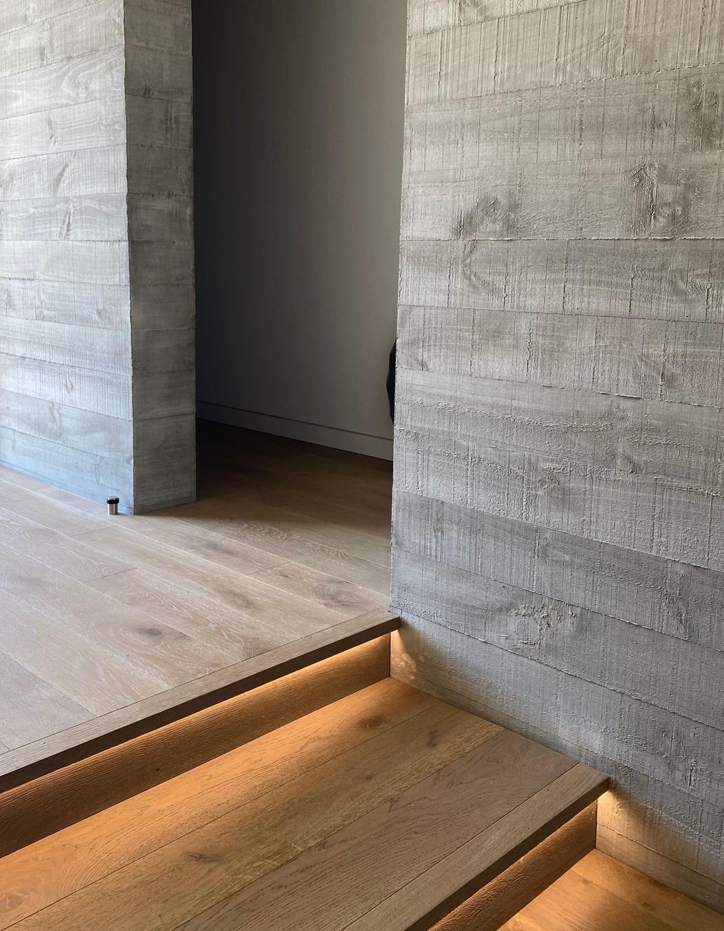Recessed lighting beneath the stair nosing highlights the warmth of the timber flooring against the concrete walls.