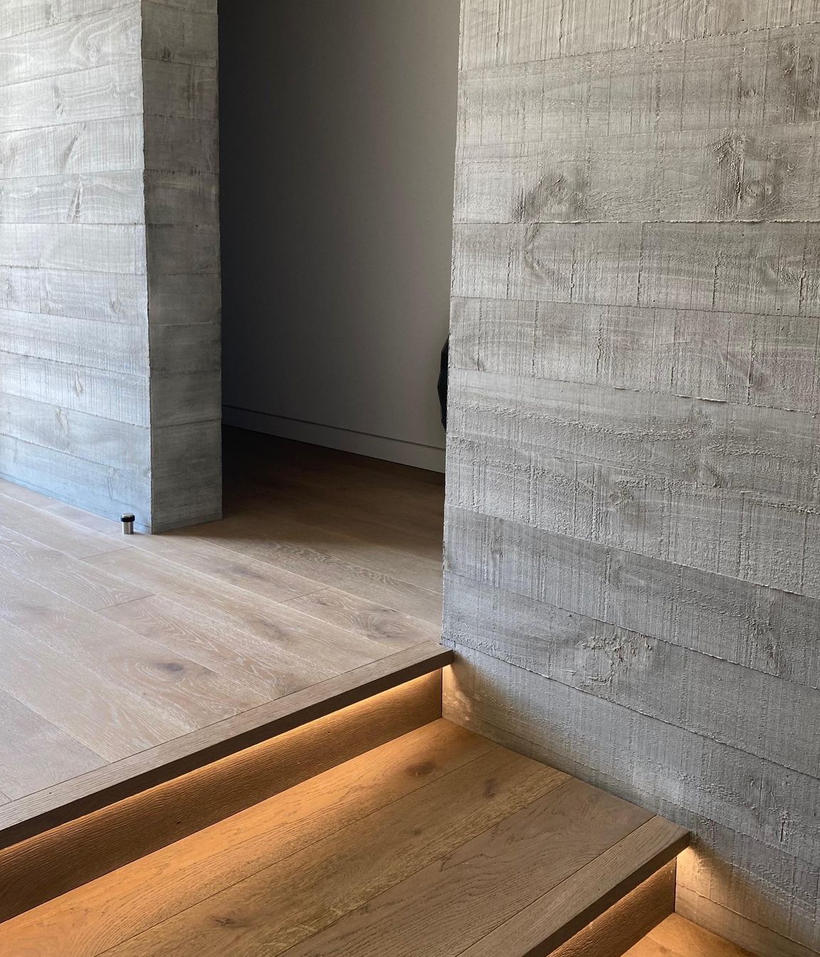 Recessed lighting beneath the stair nosing highlights the warmth of the timber flooring against the concrete walls.