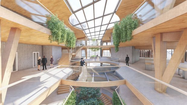 A spacious multi-level contemporary interior atrium with exposed timber structural beams and ceilings, concrete walls and floors, extensive internal glazing, and a large central skylight. Curved balustrades surround a sunken central space with integrated planting, while people provide scale. The space has abundant natural light and a civic or commercial character.