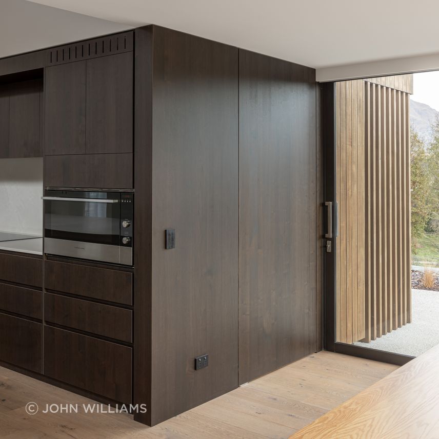 A wall of timber veneered joinery wraps around the kitchen to form a hidden door to the scullery