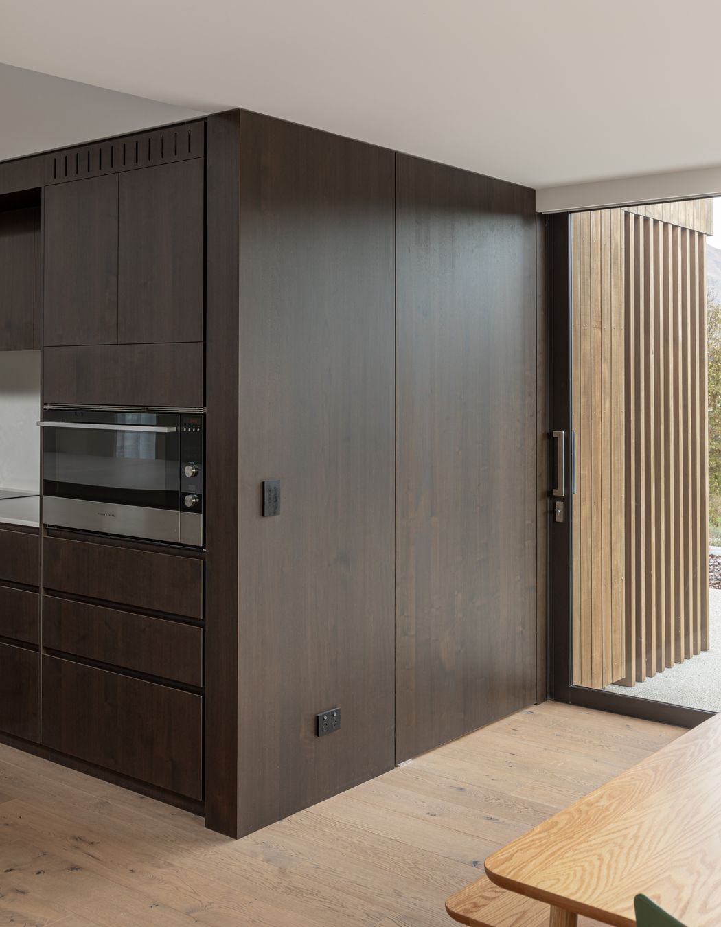 A wall of timber veneered joinery wraps around the kitchen to form a hidden door to the scullery
