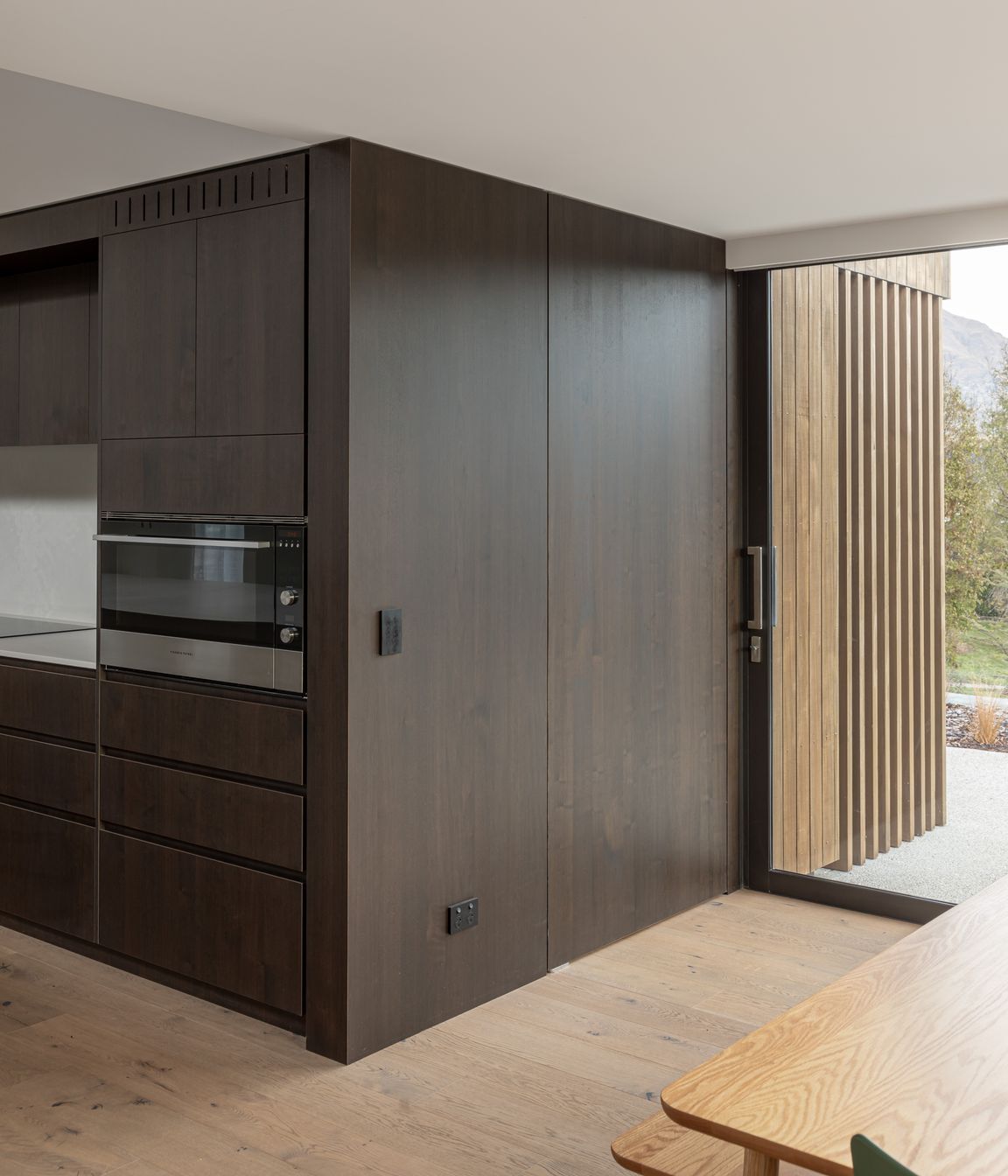 A wall of timber veneered joinery wraps around the kitchen to form a hidden door to the scullery