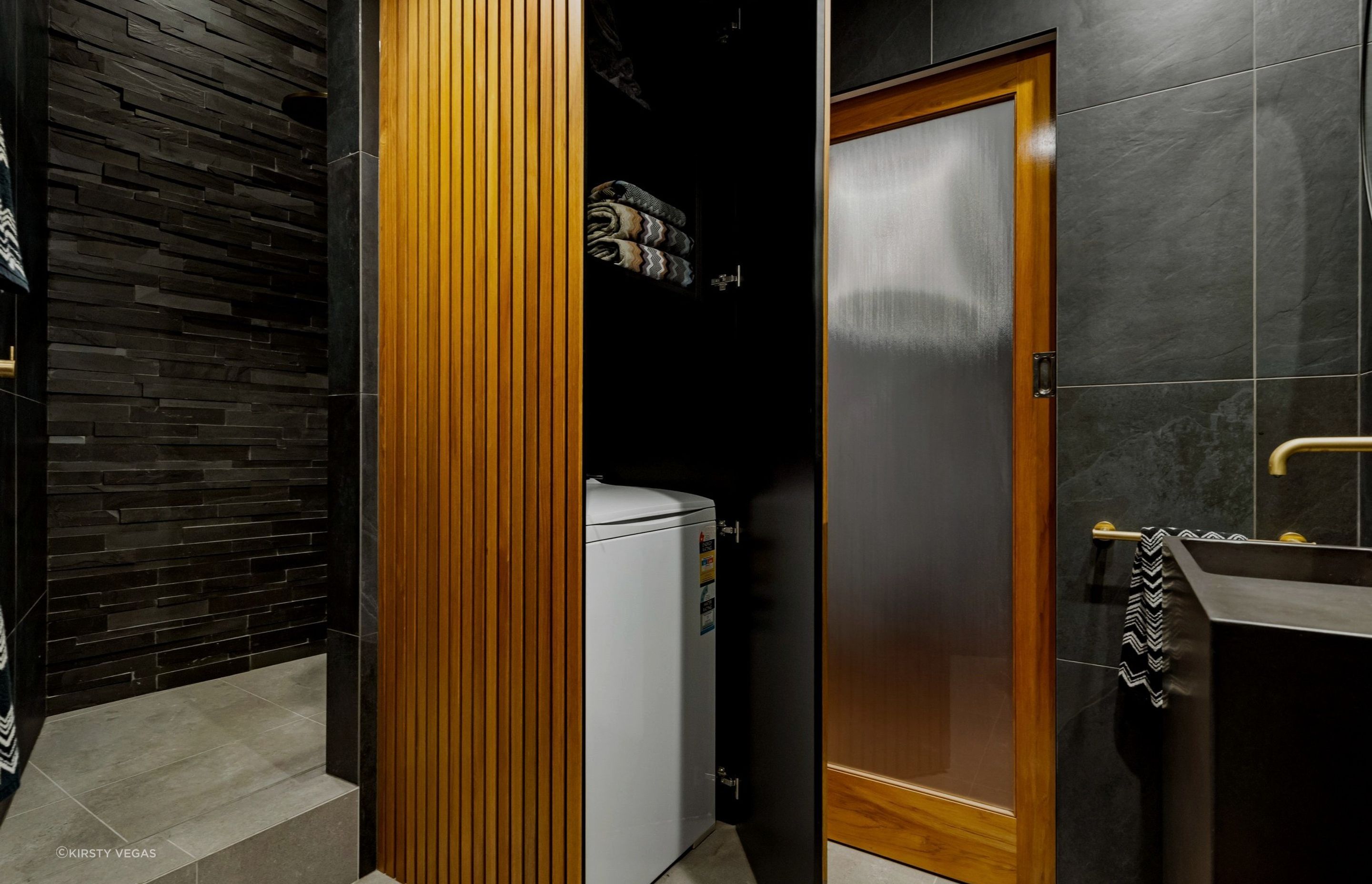 The wood-paneled cupboard discreetly hides a secret laundry space, complete with additional storage for an organized and stylish solution.