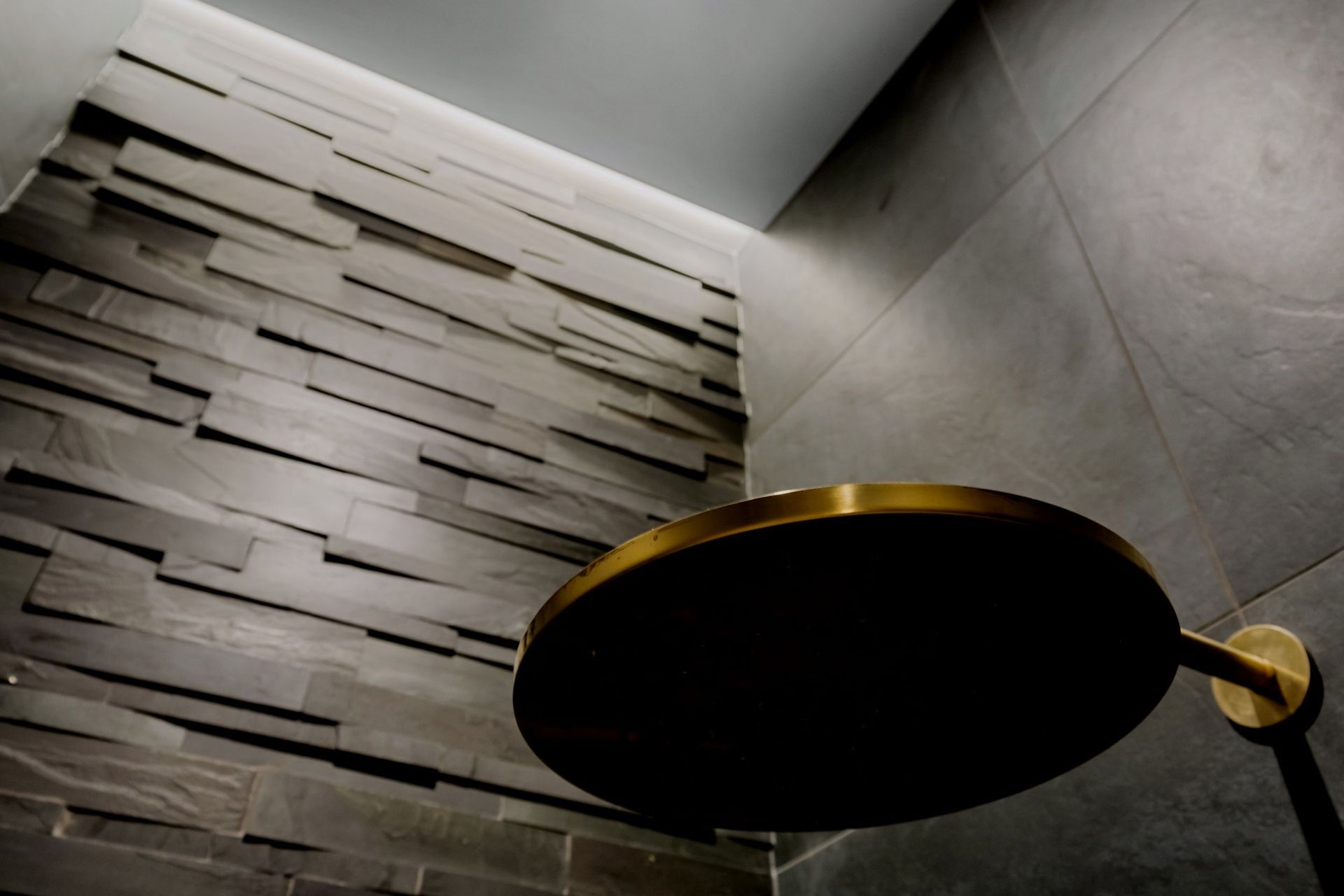 The stunning aged brass Progetto shower head creates a striking contrast against the impressive four-meter 'Island Stone' feature wall, enhancing the visual appeal of the space.