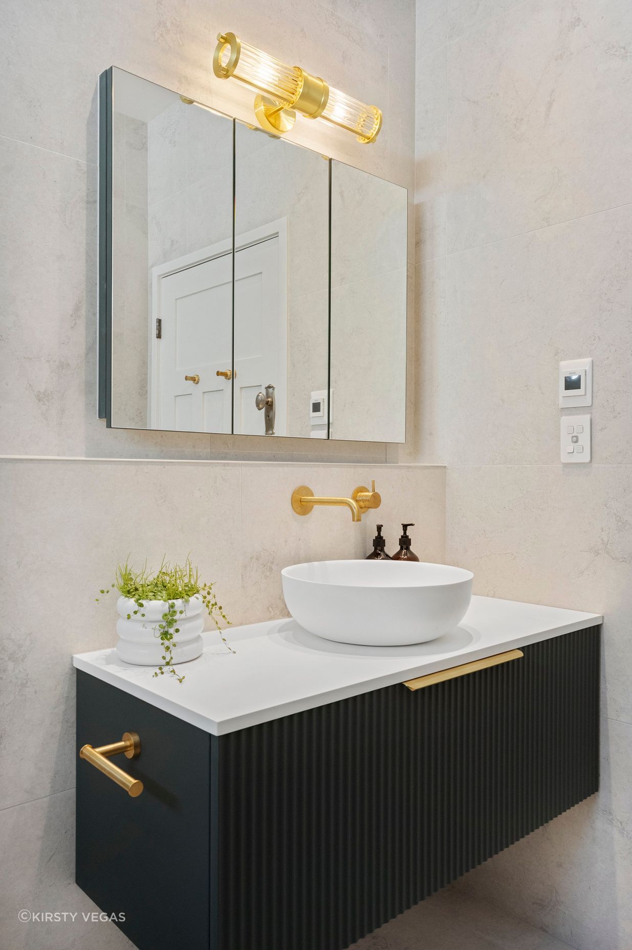 The Vista mirrored wall unit enhances the bathroom's functionality by providing additional storage and convenient power outlets, all while contributing to the sleek design. Its reflective surface amplifies natural light, creating a sense of spaciousness. Complementing this piece, the fluted glass wall lamp perfectly aligns with the fluted vanity and other brushed brass elements, creating a cohesive and harmonious aesthetic. Together, these features add both practicality and style, elevating the overall elegance of the bathroom.