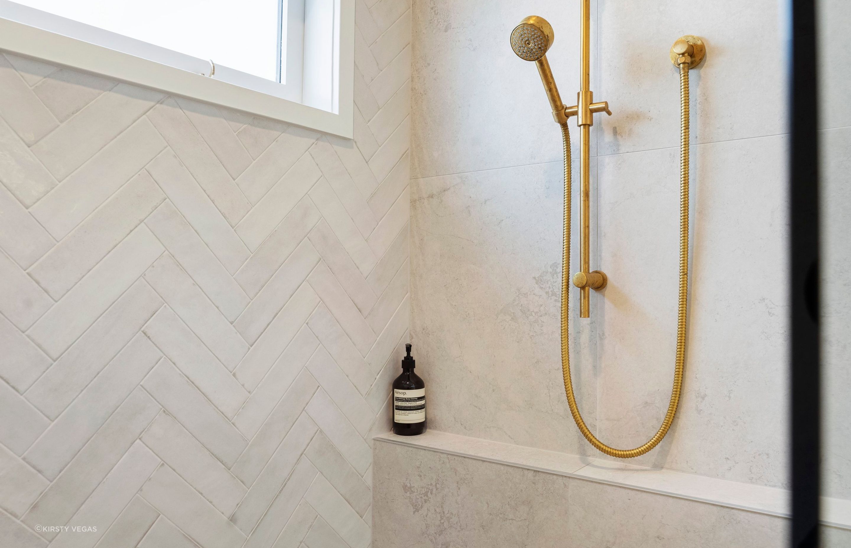 The Tribeca Gypsum white herringbone tiles on the back wall introduce a beautiful texture and understated visual interest to the space, setting the perfect stage for the Progetto organic brushed brass shower head to stand out. The elegant pattern of the tiles enhances the overall aesthetic, creating a soft, contemporary backdrop that beautifully contrasts with the warm tones of the brass fixture. This thoughtful design choice not only elevates the shower area but also adds a touch of sophistication, making it a stunning focal point in the bathroom.