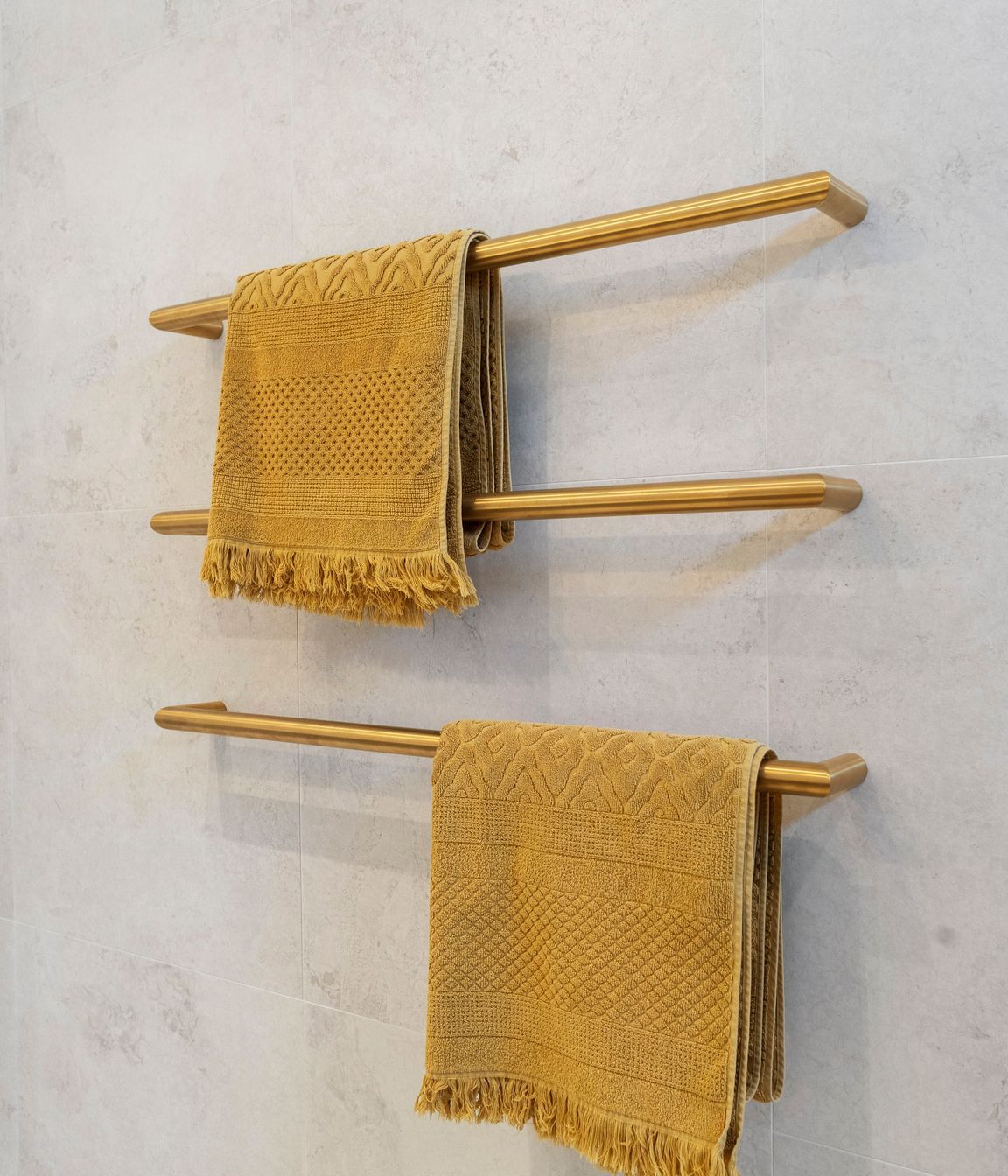 The individual brushed brass heated towel rails are a strikingly elegant yet minimalist addition to the bathroom, perfectly contrasting against the Breccia white matt wall tiles. Their sleek design not only enhances the aesthetic appeal of the space but also provides practical warmth and comfort. The warmth of the brass against the crisp white tiles creates a sophisticated interplay of color and texture, elevating the overall elegance of the bathroom while ensuring functionality and style.
