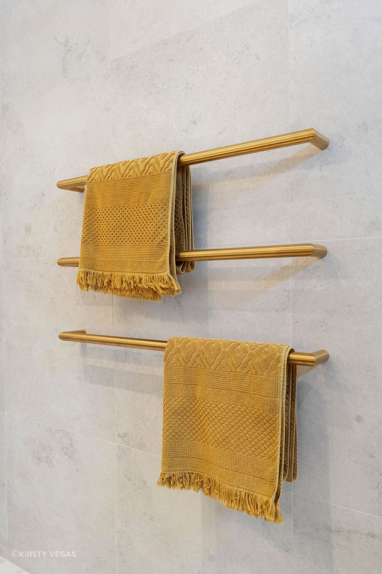 The individual brushed brass heated towel rails are a strikingly elegant yet minimalist addition to the bathroom, perfectly contrasting against the Breccia white matt wall tiles. Their sleek design not only enhances the aesthetic appeal of the space but also provides practical warmth and comfort. The warmth of the brass against the crisp white tiles creates a sophisticated interplay of color and texture, elevating the overall elegance of the bathroom while ensuring functionality and style.