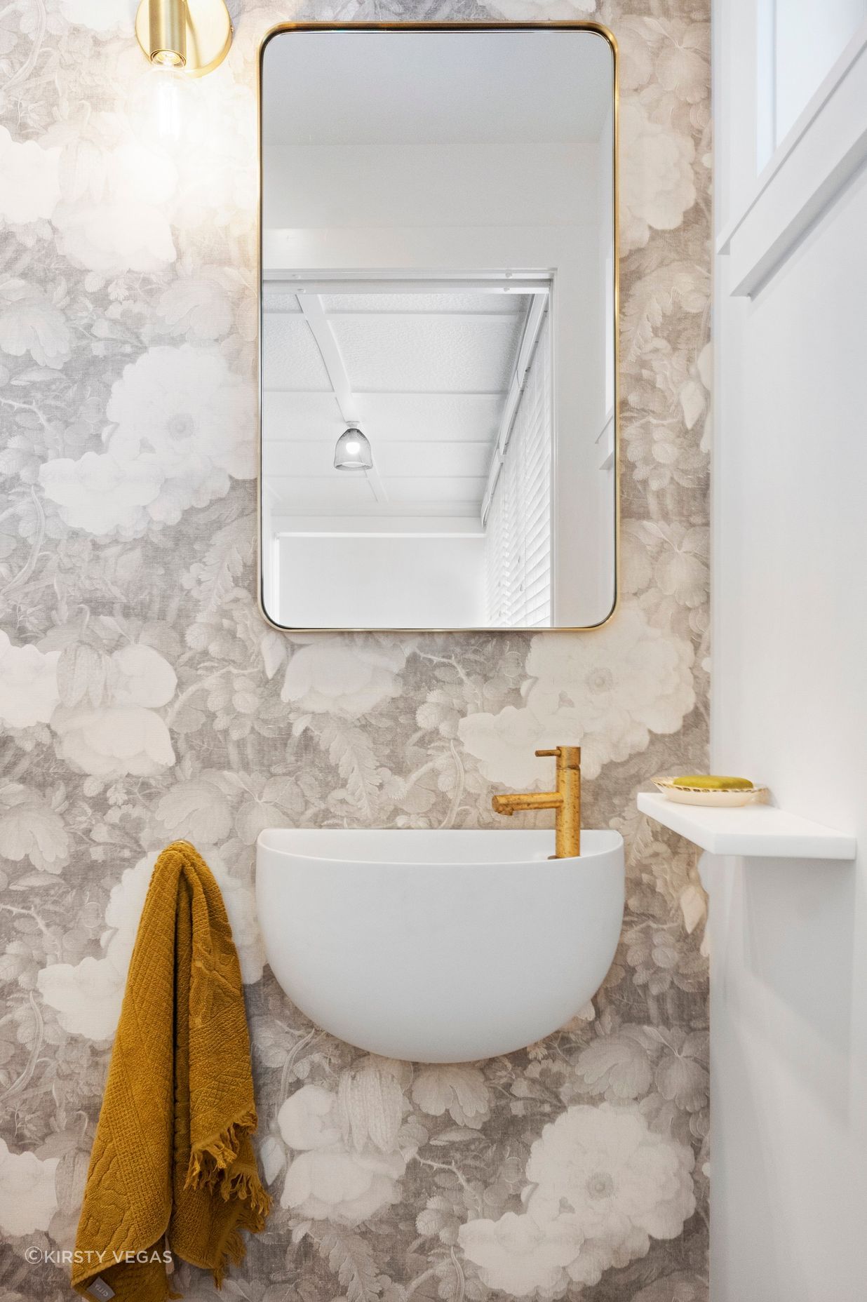 The stunning curved wall-hung Lavamani round basin harmoniously complements the custom linen wallpaper, creating a seamless blend of elegance and artistry. Its graceful shape adds visual interest and softens the overall aesthetic, while the intricate floral patterns of the wallpaper enhance the basin's refined design. Together, they create a beautifully curated focal point in the powder room, infusing the space with a sense of style and tranquility.