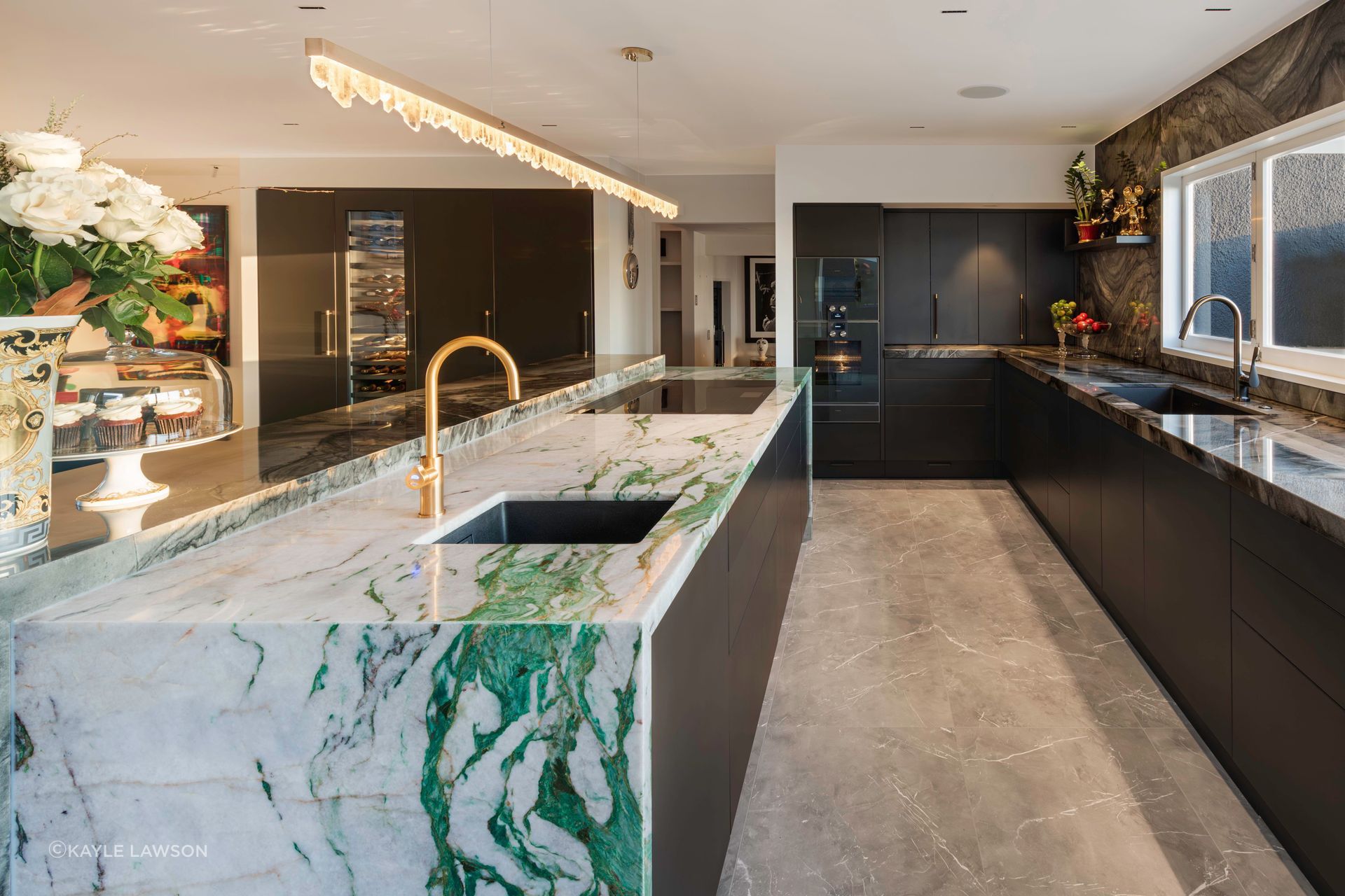 The same stormy charcoal stone is used on the sink bench and walls for a moody textural backdrop to everchanging harbour views. A metal-infused black lacquer is specified for the kitchen’s joinery while anthracite and brass tapware and soft oyster floor tiles complete the rich palette. The double sinks, fridge, three ovens including a sous vide, and pantry storage are perfectly arranged within the hob-centred zone to allow the home chef efficient flow and access.