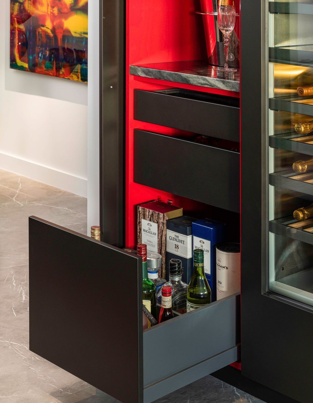 Opening the wine bar door reveals a treasure box of magic.  A splash of “Jalapeno” nail-polish red is rendered in a glamorous gloss finish to emphasize its sophistication and delight the senses.   With the door pocketed away, a compilation of glass shelving, a stone bench top, drawers for spirits, bar snacks and black felt-lined drawers are all beautifully detailed, fittingly enough to remain open.