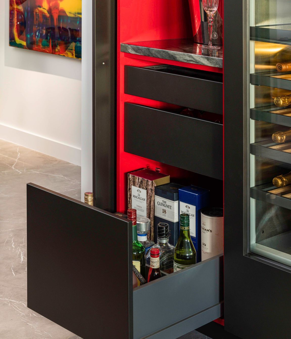 Opening the wine bar door reveals a treasure box of magic.  A splash of “Jalapeno” nail-polish red is rendered in a glamorous gloss finish to emphasize its sophistication and delight the senses.   With the door pocketed away, a compilation of glass shelving, a stone bench top, drawers for spirits, bar snacks and black felt-lined drawers are all beautifully detailed, fittingly enough to remain open.