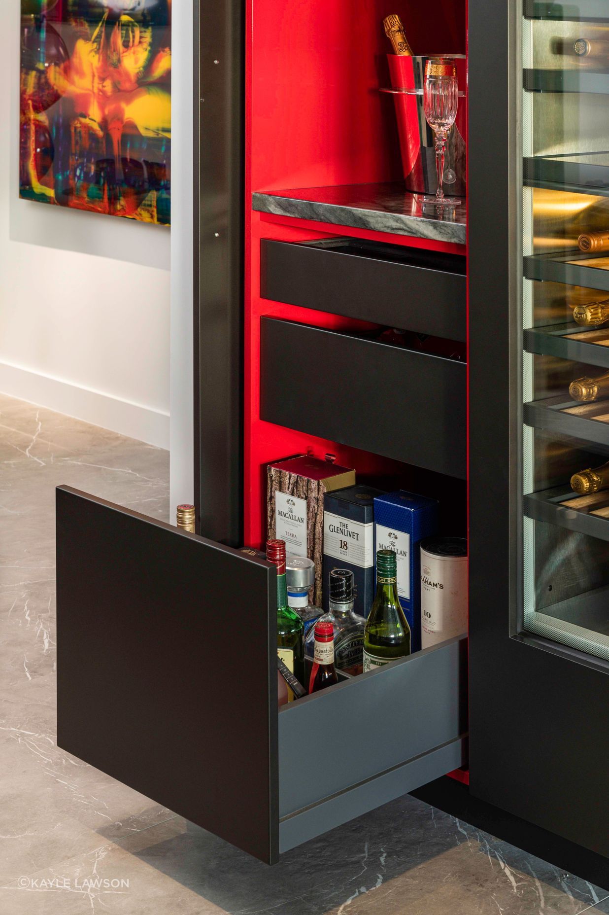 Opening the wine bar door reveals a treasure box of magic. A splash of “Jalapeno” nail-polish red is rendered in a glamorous gloss finish to emphasize its sophistication and delight the senses. With the door pocketed away, a compilation of glass shelving, a stone bench top, drawers for spirits, bar snacks and black felt-lined drawers are all beautifully detailed, fittingly enough to remain open.