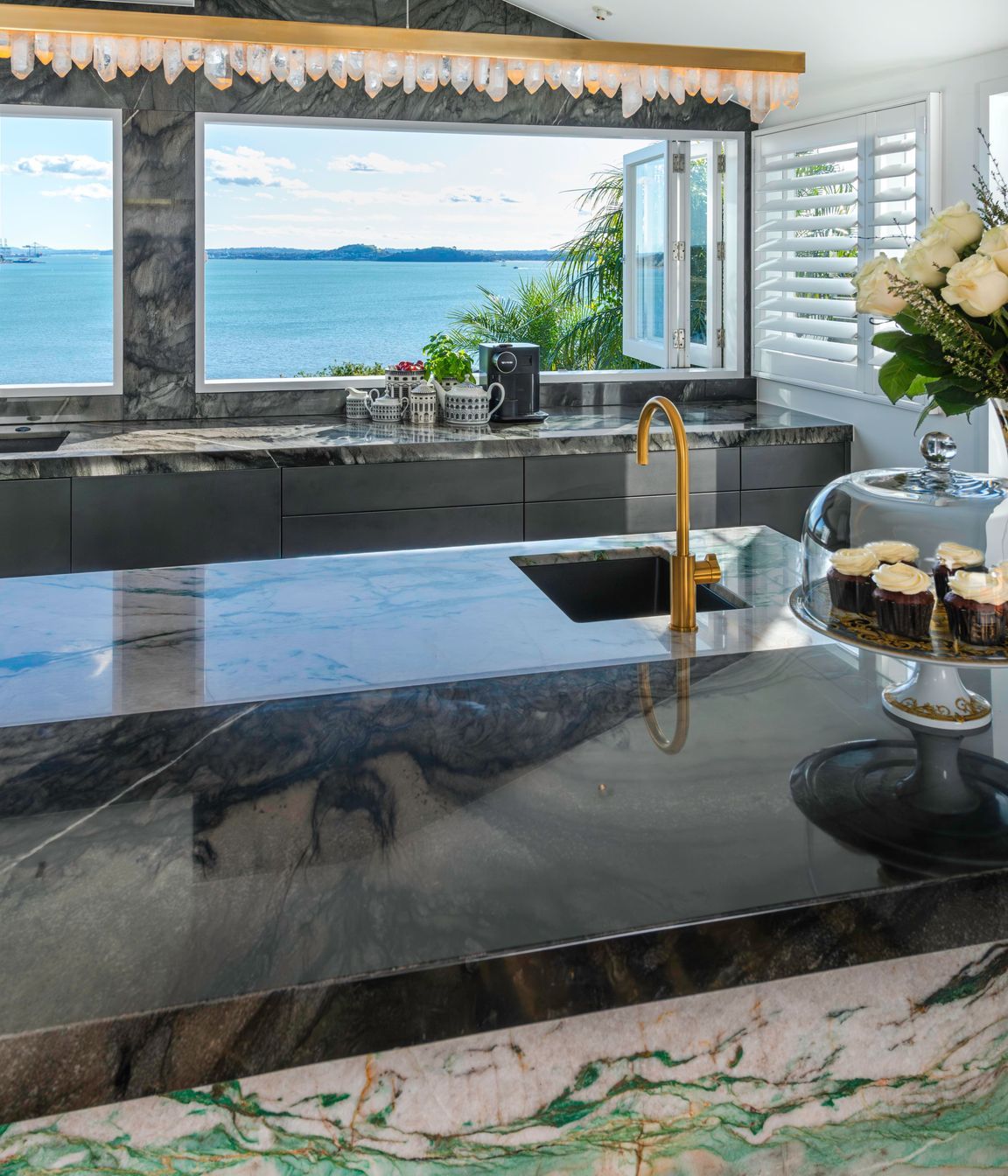 A daytime drinks area is centered around a brass-rendered tap dispensing chilled, sparkling and boiling water on the island. Related coffee cups, teas boxes and glasses are stored in touch-motion drawers opposite.  Several custom-dimensioned drawers hosting the owners’ extensive dinnerware and serveware collections, are positioned conveniently beside the dishwasher.