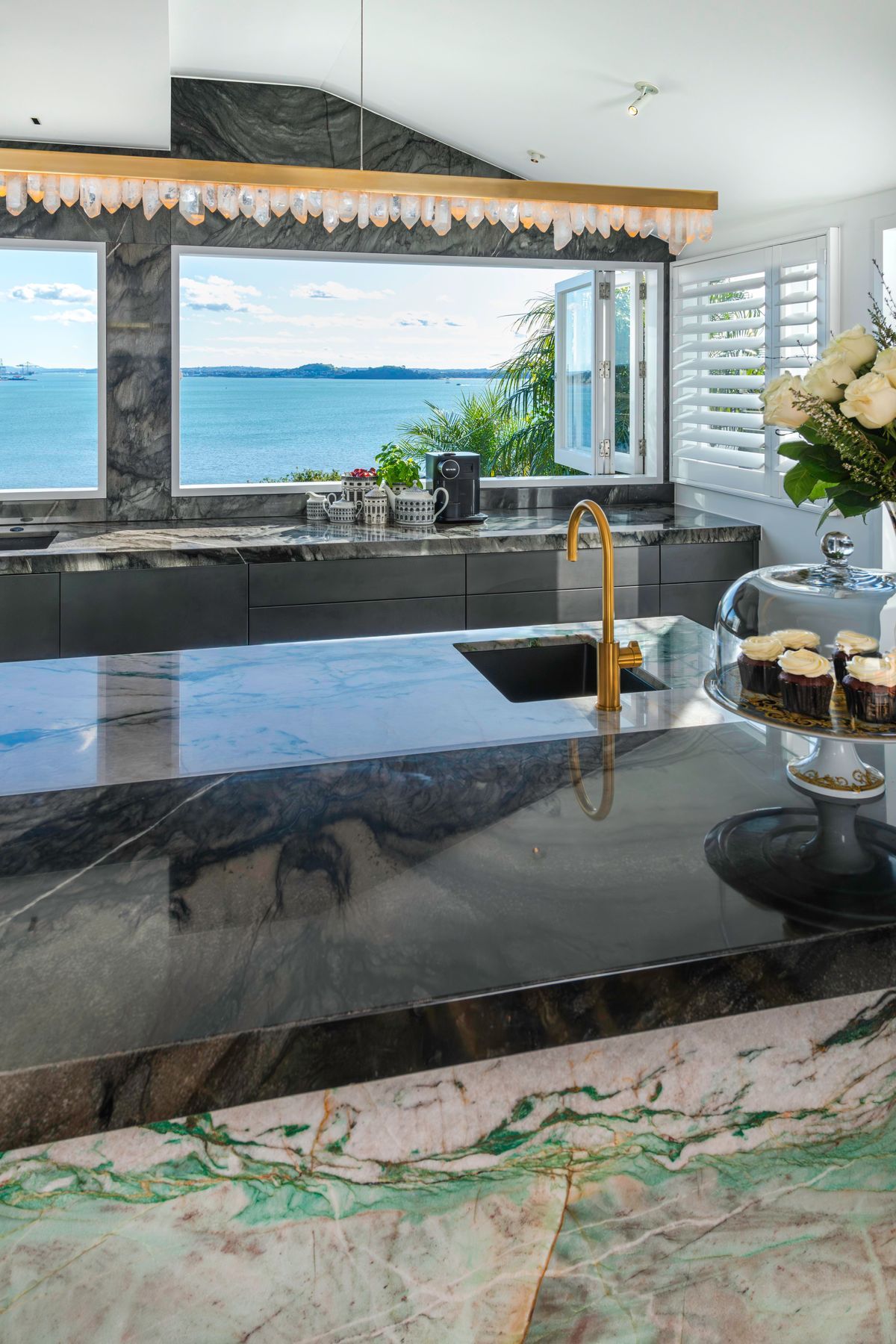 A daytime drinks area is centered around a brass-rendered tap dispensing chilled, sparkling and boiling water on the island. Related coffee cups, teas boxes and glasses are stored in touch-motion drawers opposite. Several custom-dimensioned drawers hosting the owners’ extensive dinnerware and serveware collections, are positioned conveniently beside the dishwasher.