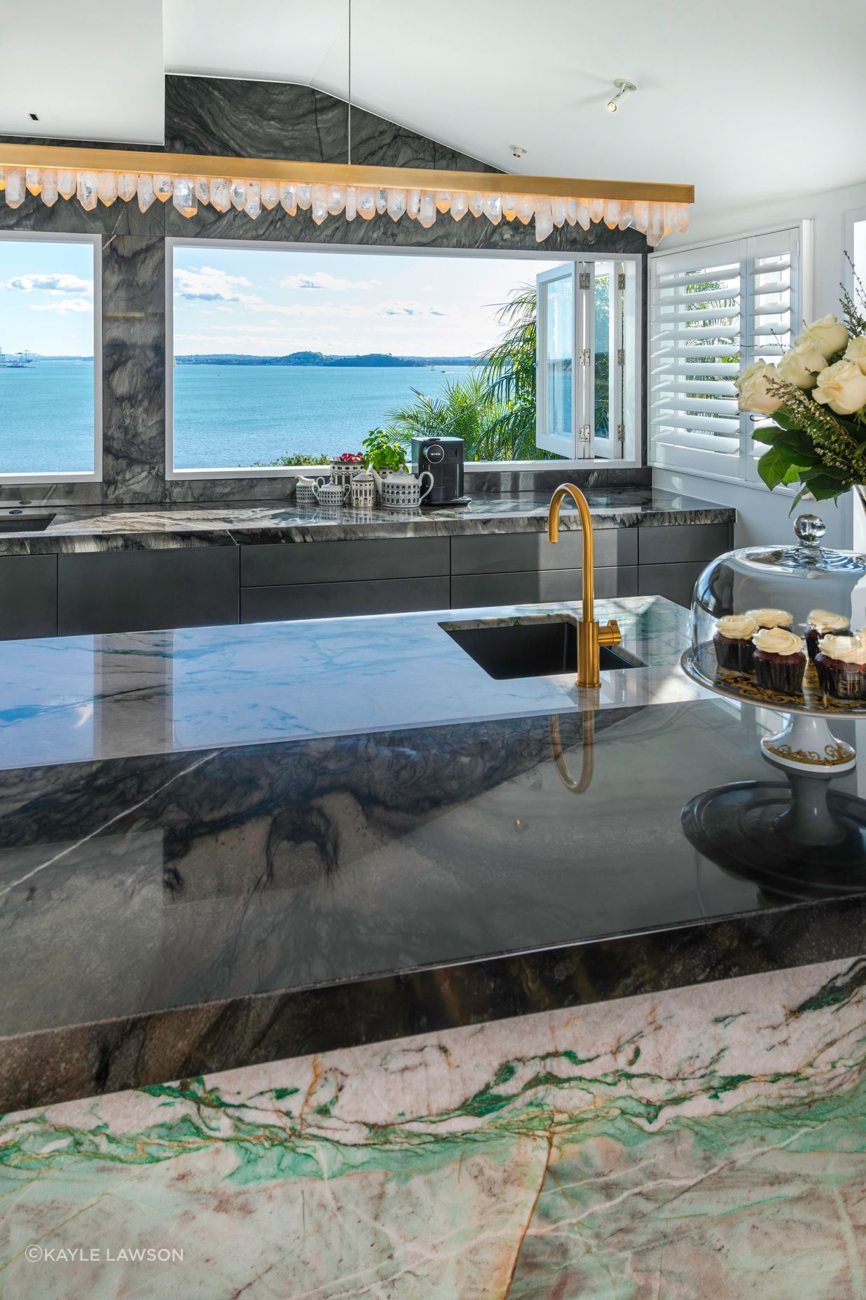 A daytime drinks area is centered around a brass-rendered tap dispensing chilled, sparkling and boiling water on the island. Related coffee cups, teas boxes and glasses are stored in touch-motion drawers opposite. Several custom-dimensioned drawers hosting the owners’ extensive dinnerware and serveware collections, are positioned conveniently beside the dishwasher.
