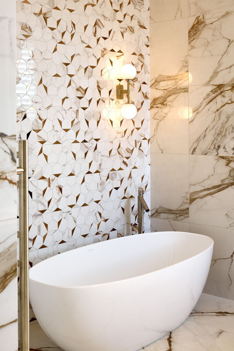 An oval freestanding bath creates a sculptural focal point within the ensuite. Marble-look floor and wall tiles wrap the space in a calm and cohesive material palette.
