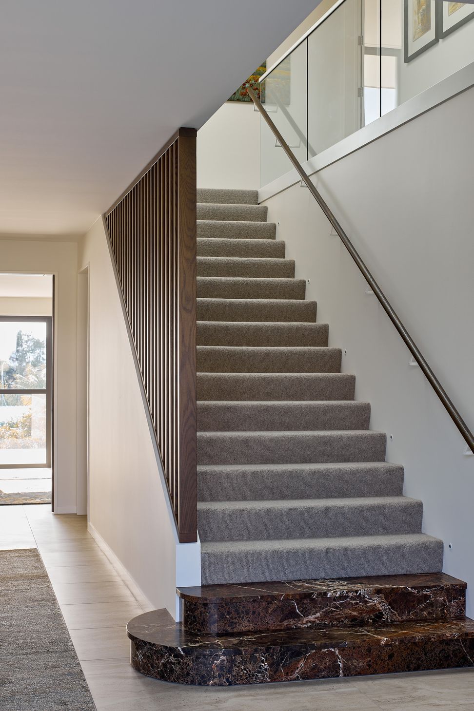 The spacious entrance hall creates a generous sense of arrival, with the staircase forming a sculptural connection between the home's three levels. Natural stone, timber and tiled finishes establish the material language used throughout the house.