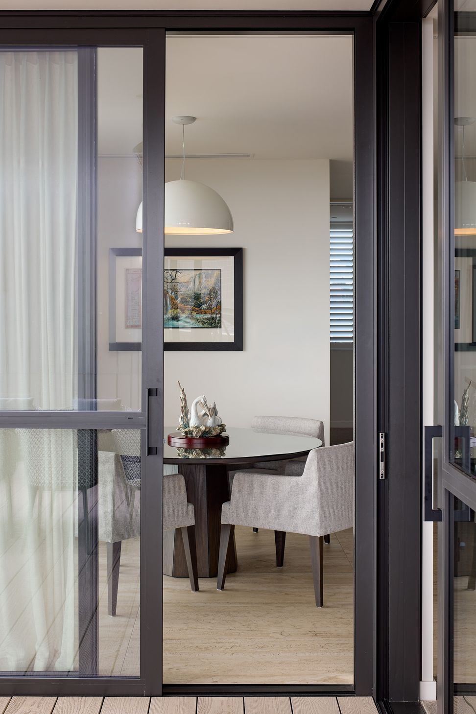 Viewed from the deck, the informal dining area forms an intimate gathering place within the larger open-plan living space. A sculptural pendant light creates a focal point above the round dining table.