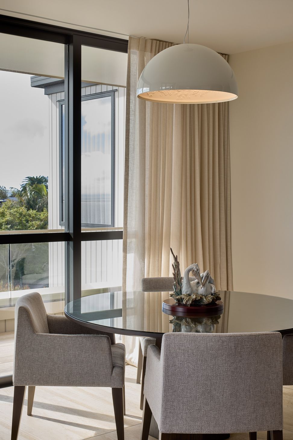 The informal dining area is positioned beside the deck to make the most of natural light and the coastal outlook. A sculptural pendant creates a warm focal point, while views extend beyond the table towards the Hauraki Gulf.