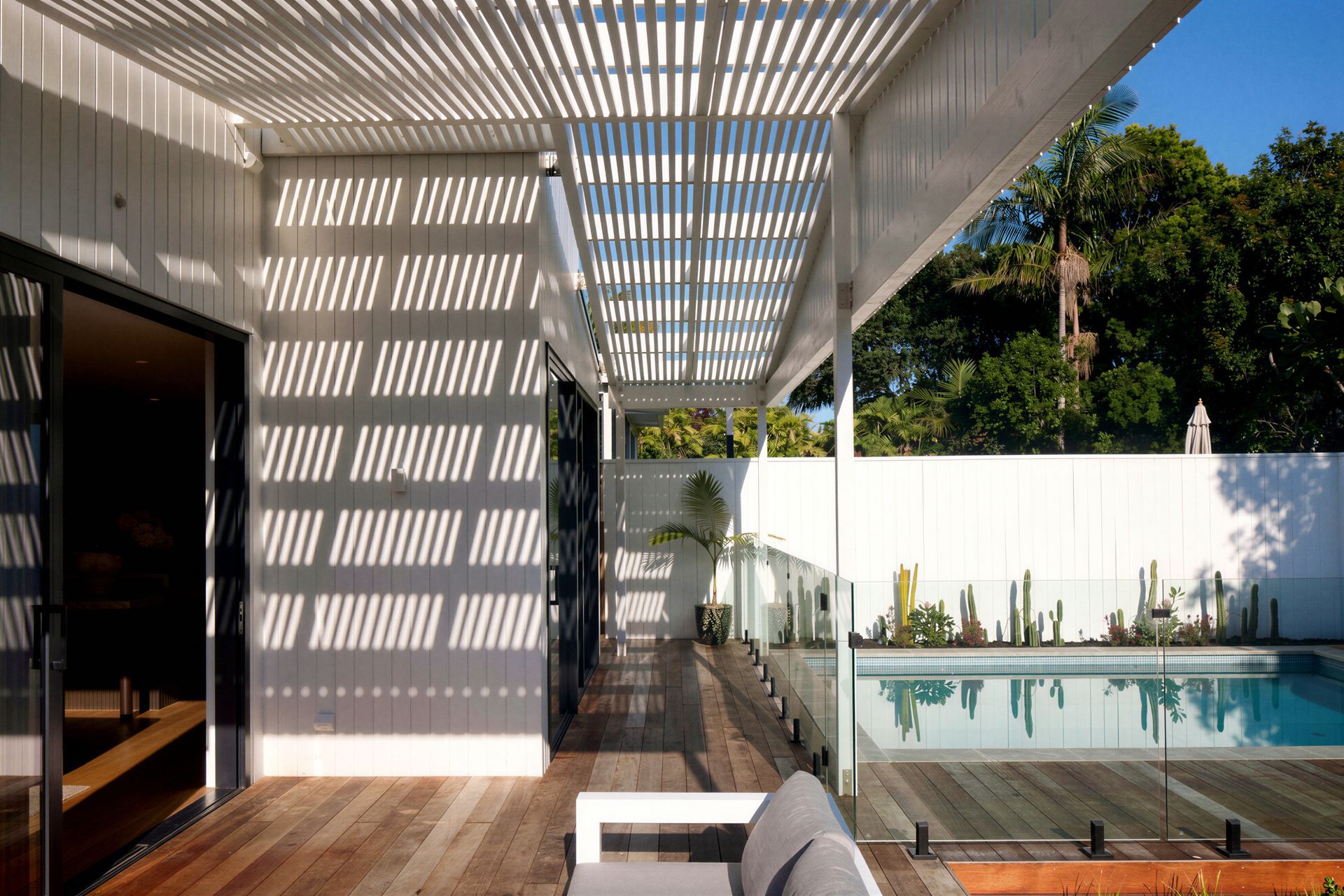 The covered outdoor lounge extends the home's living spaces into the garden. Sheltered beneath a slatted pergola, the deck overlooks the swimming pool while large sliding doors create a seamless connection back to the interior.
