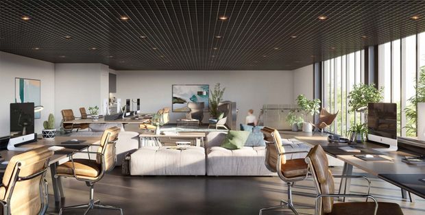 A bright, expansive open-plan contemporary interior combining a lounge area with multiple workstations. A light sectional sofa, glass coffee table, leather-and-chrome chairs, desks with computer monitors, indoor plants, artwork, and large floor-to-ceiling windows define the space. The dark exposed grid ceiling and dark flooring create contrast with the pale upholstery and abundant daylight.