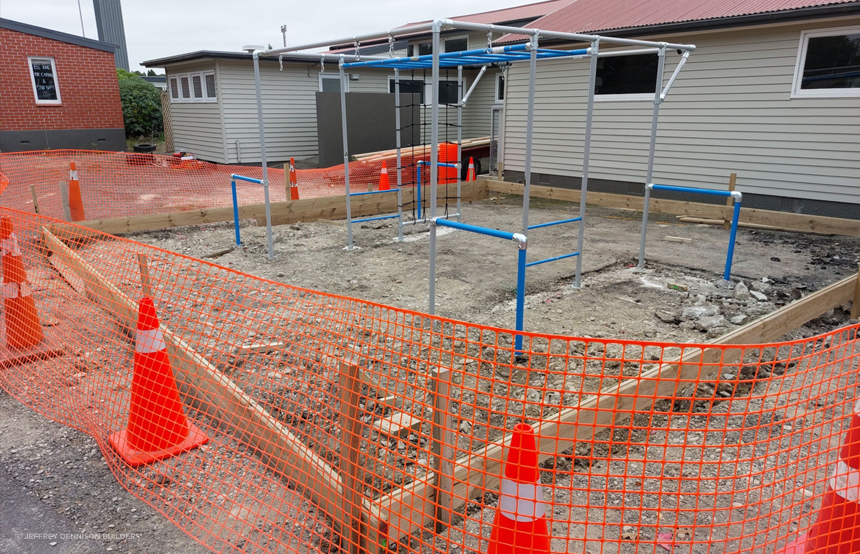 Monkey bars being erected and bolted to the foundation, image also shows timber profile being constructed to hold the bark chips inside.