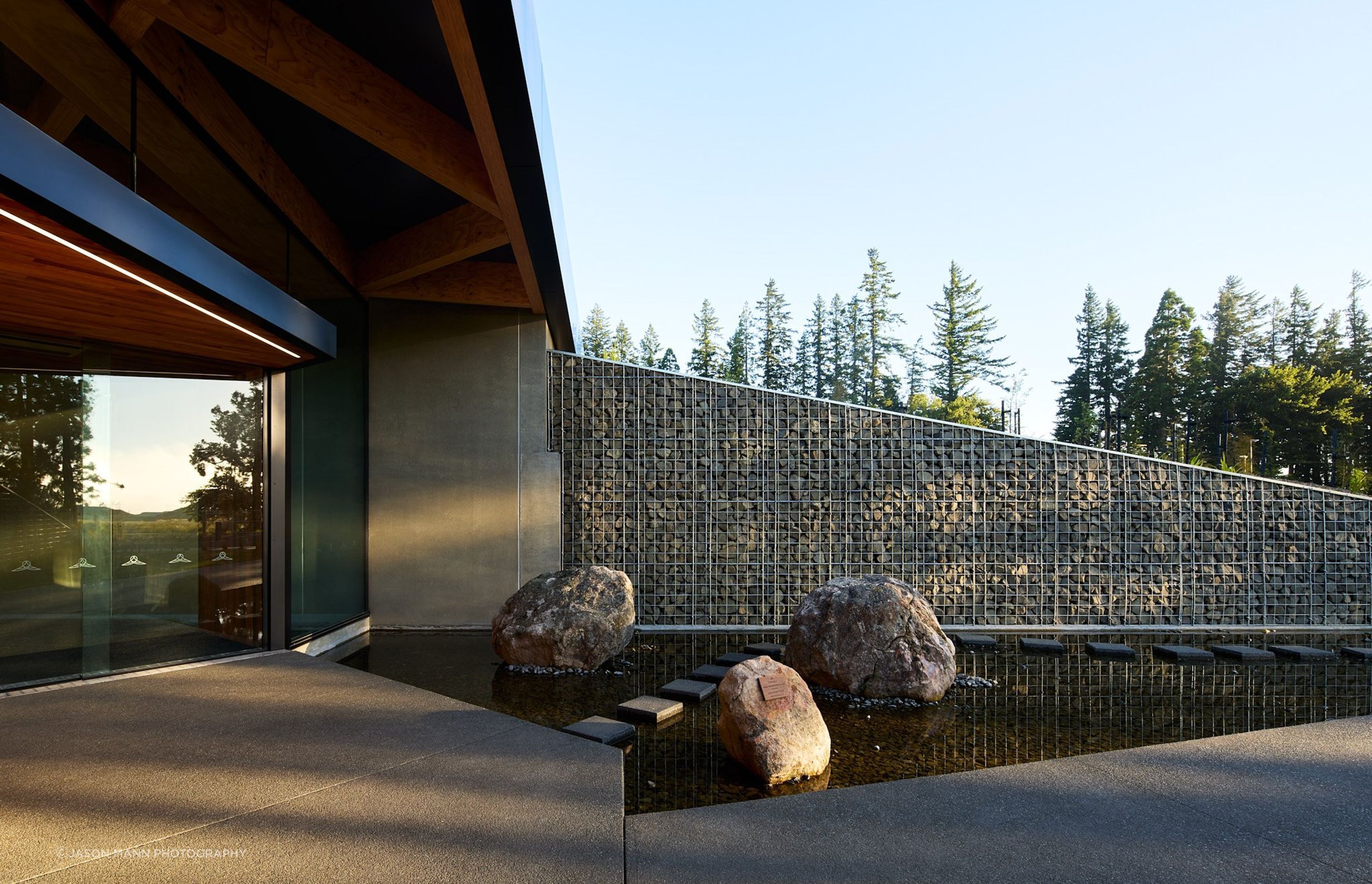 The entry to the complex features gabion walls and a water feature, narrowing into the entranceway.