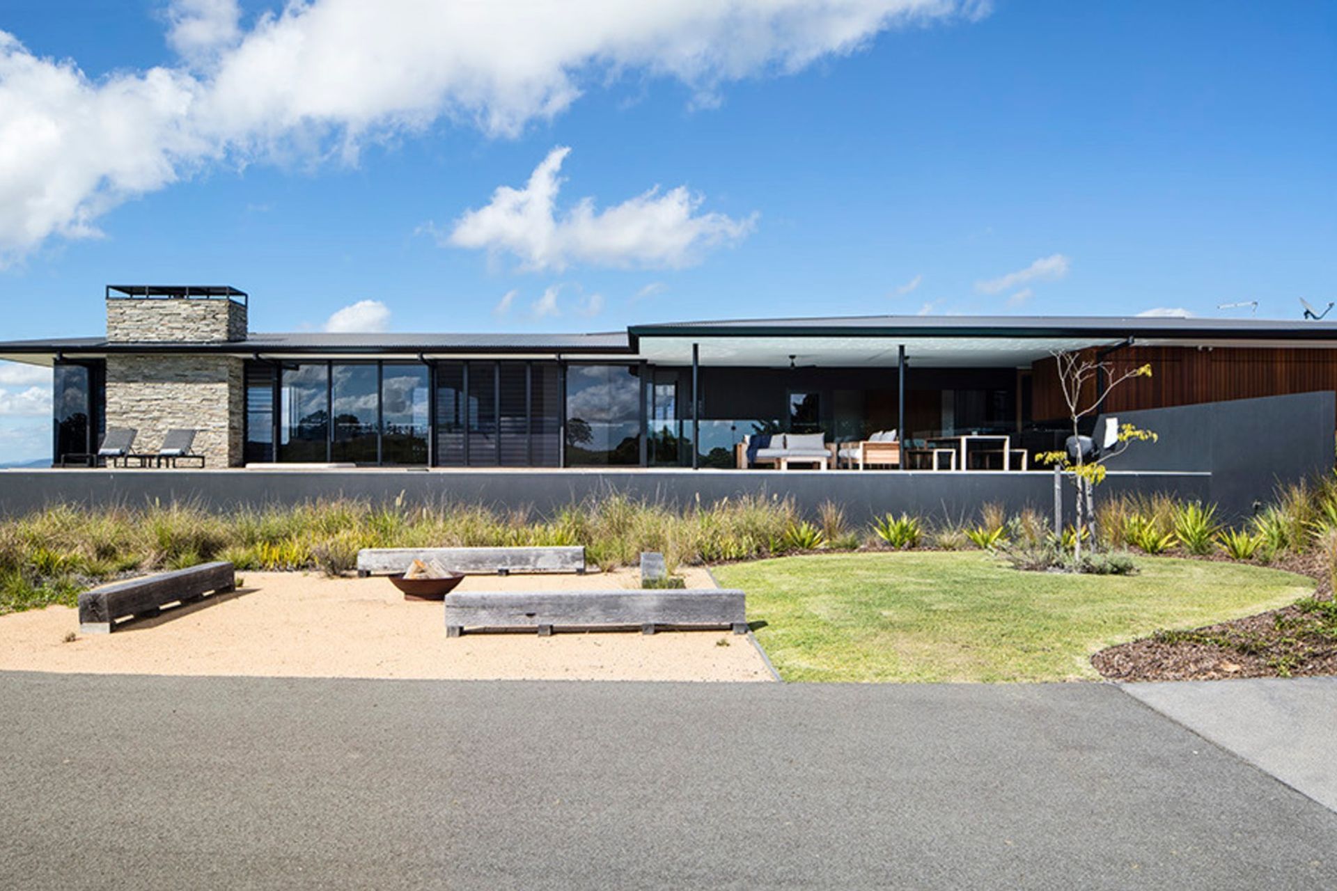 Clark Residence - Exterior. Stone chimney and long low roof above native grasses.