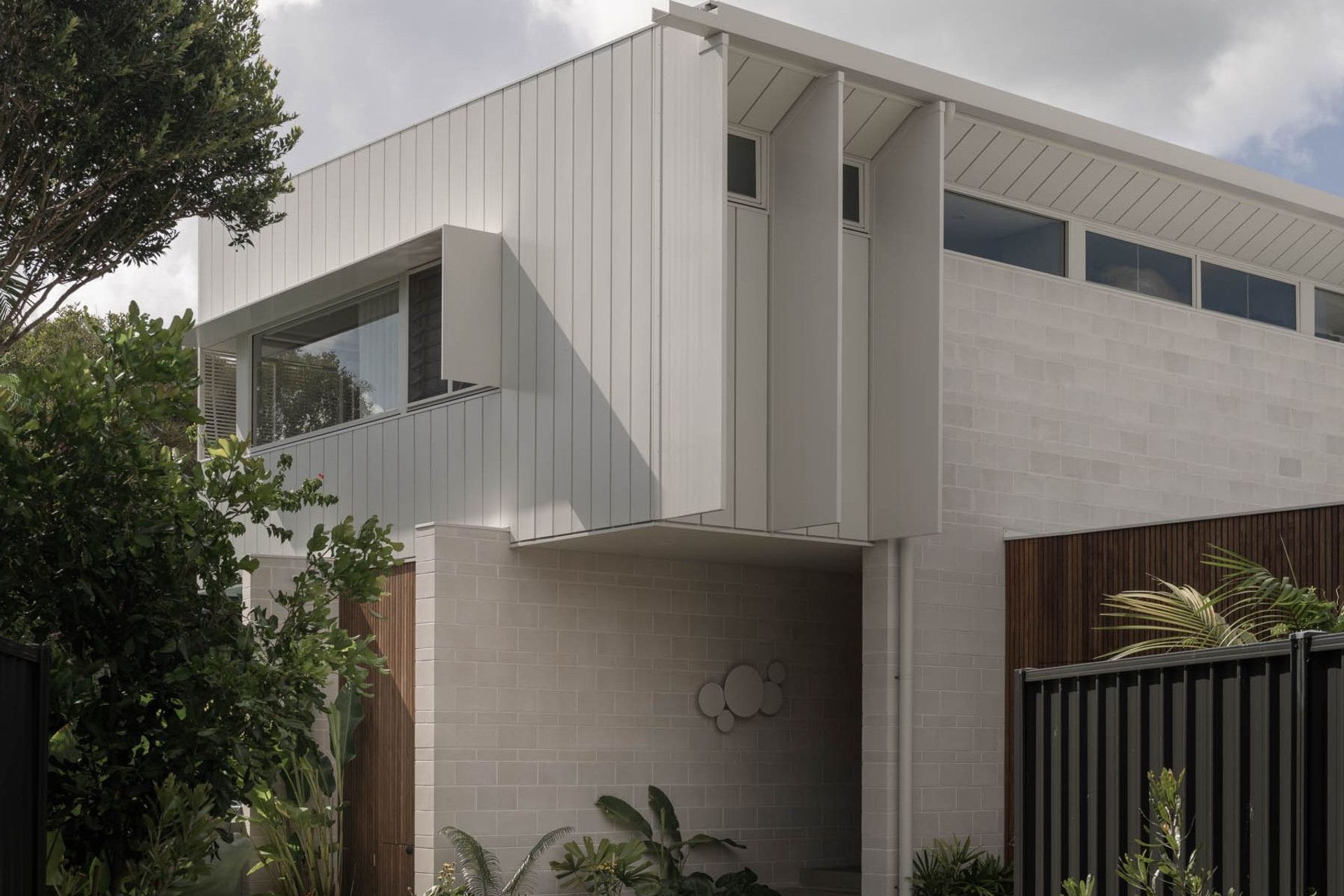 Eleutheria - Exterior. Perforated metal clad upper level floating above a pale block base.