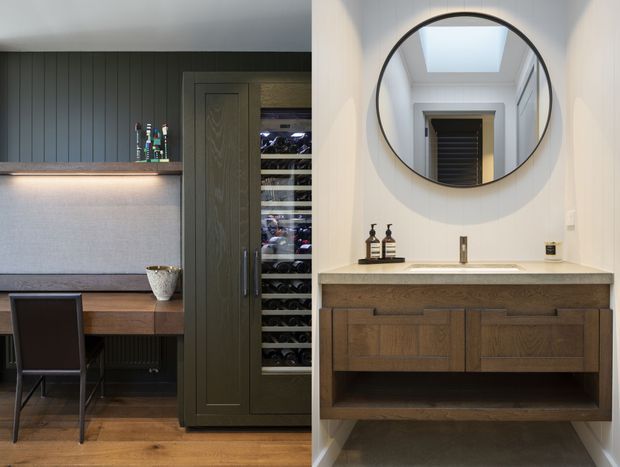 A refined residential interior combining a compact home office with a concealed wine storage cabinet and an adjacent bathroom vanity. The left side features dark vertical wall panelling, a timber desk, chair, integrated lighting and a tall glazed wine cabinet. The right side has a timber floating vanity with a pale stone benchtop, round black-framed mirror, wall-mounted tap and a skylight reflected in the mirror. The palette is warm timber, charcoal, white and grey, with clean contemporary detailing.