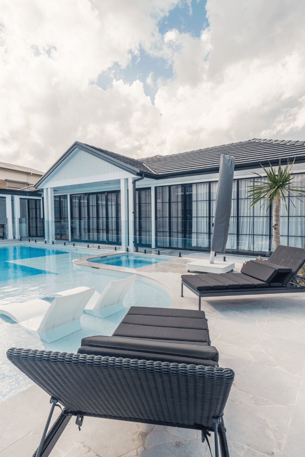 Glass walls open the living spaces to the pool, with Luna Chiaro Limestone flowing seamlessly from indoor to outdoor. The stone's neutral palette and Alfresco finish create a calm, cohesive backdrop for relaxed coastal living.