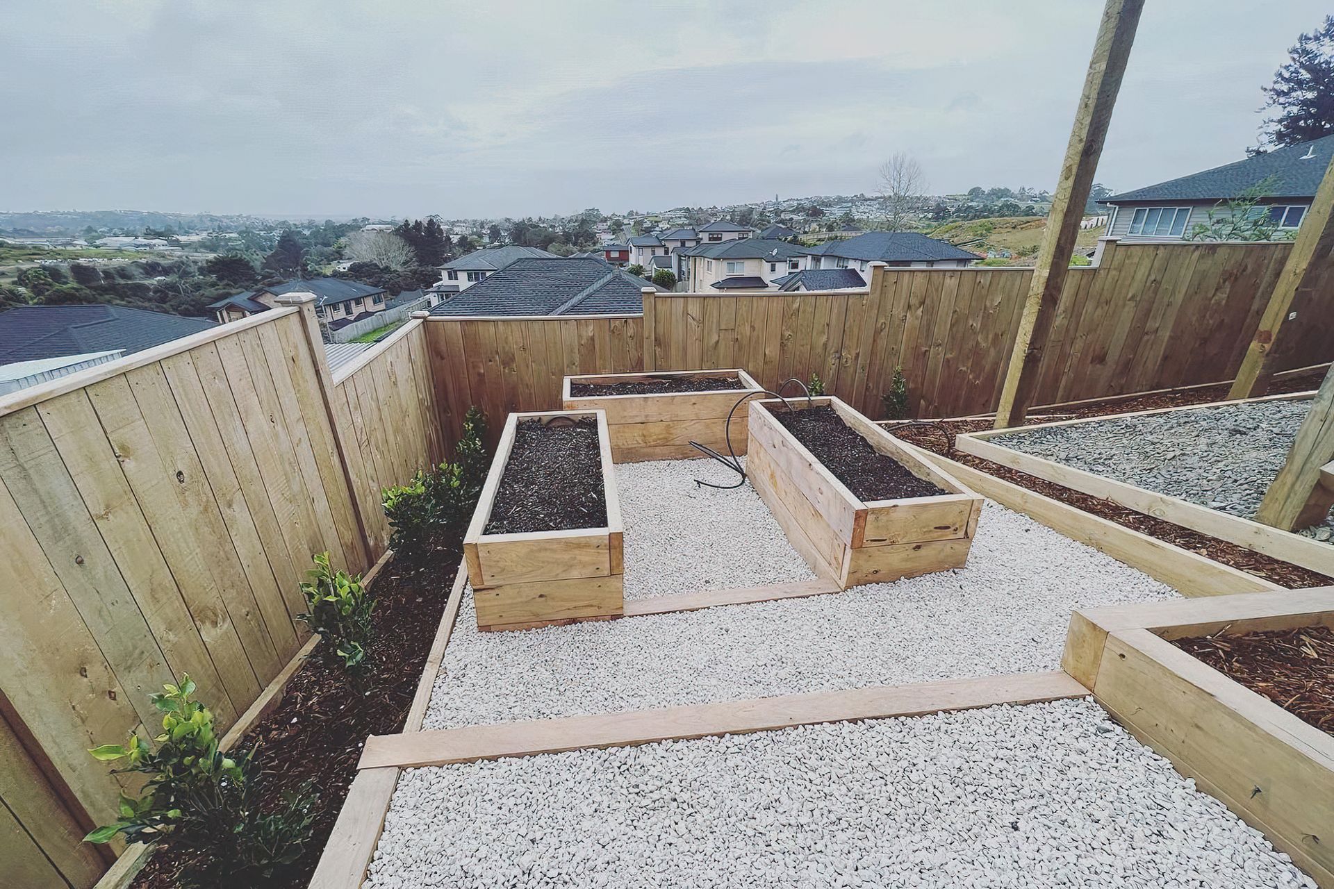 Three newly built vegetable beds raised off the ground in wood casings, surrounded by a white pebble walkway