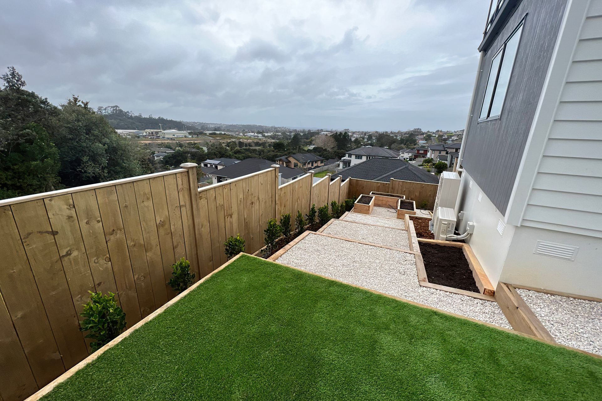North Shore backyard with a green square of grass and several large steps covered in pebbles held up by wood retaining walls