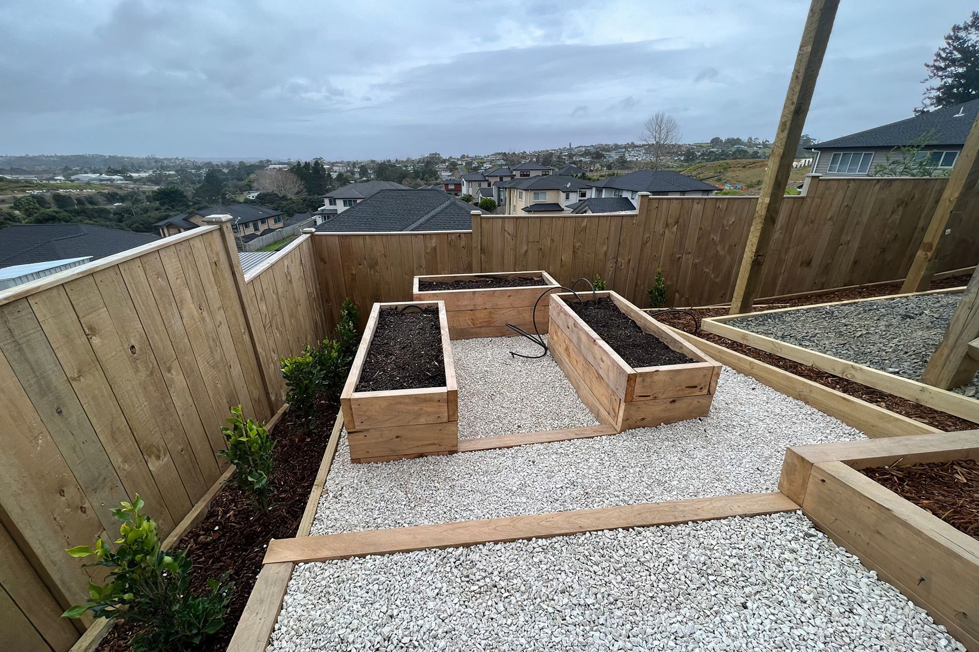 Three newly built vegetable beds raised off the ground in wood casings, surrounded by a white pebble walkway